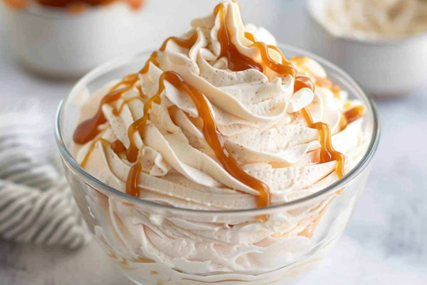 Salted caramel whipped cream drizzled with caramel syrup on a glass bowl.