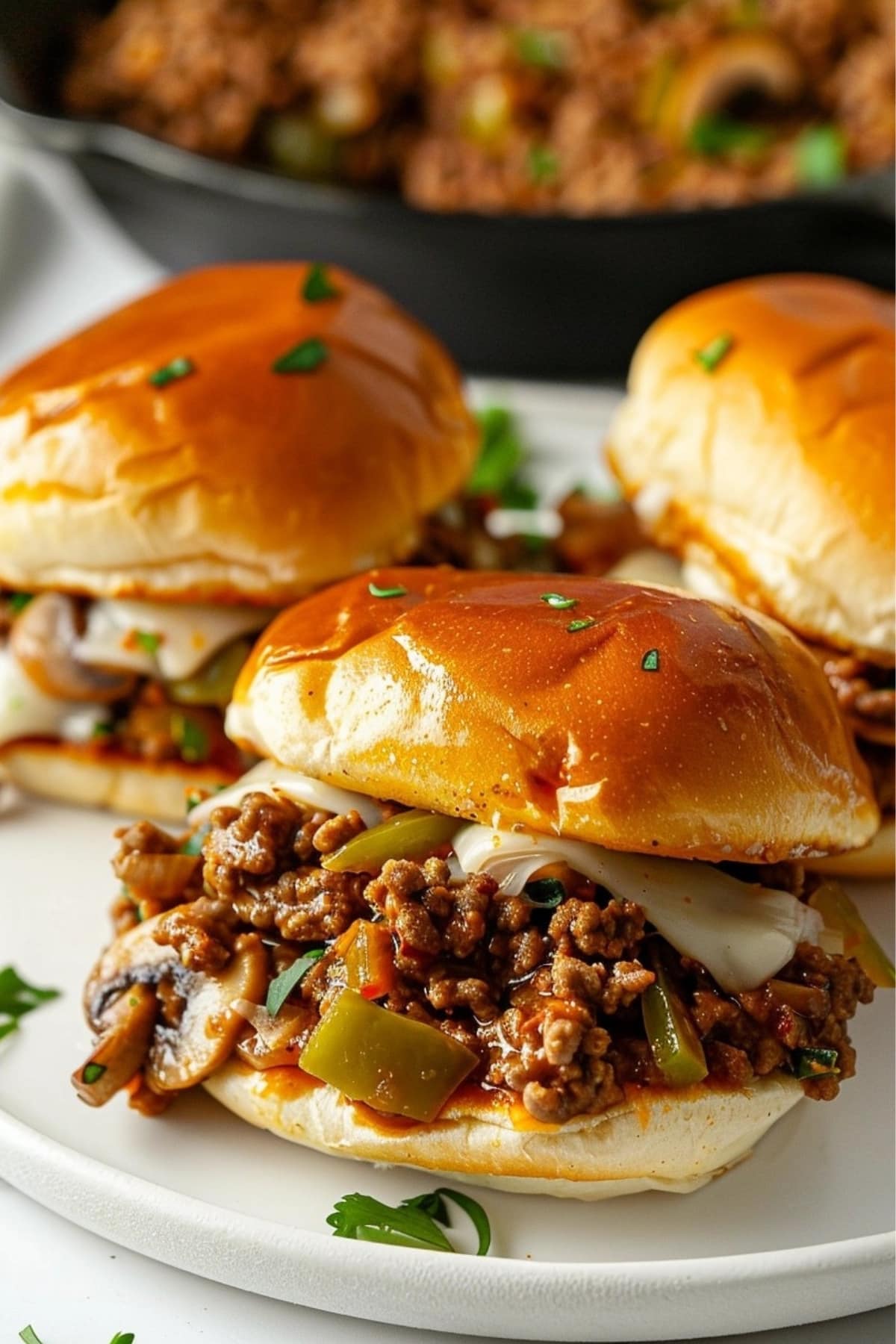 Philly Cheesesteak Sloppy Joes in a white plate, cast iron with fillings in the background.