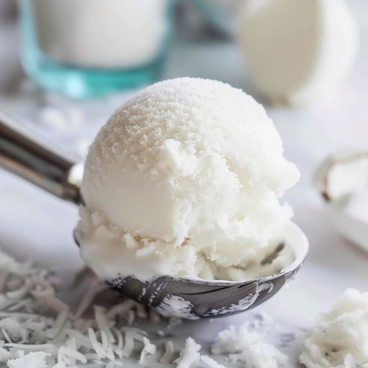 Ice cream scoop with coconut sorbet on a white marble table.