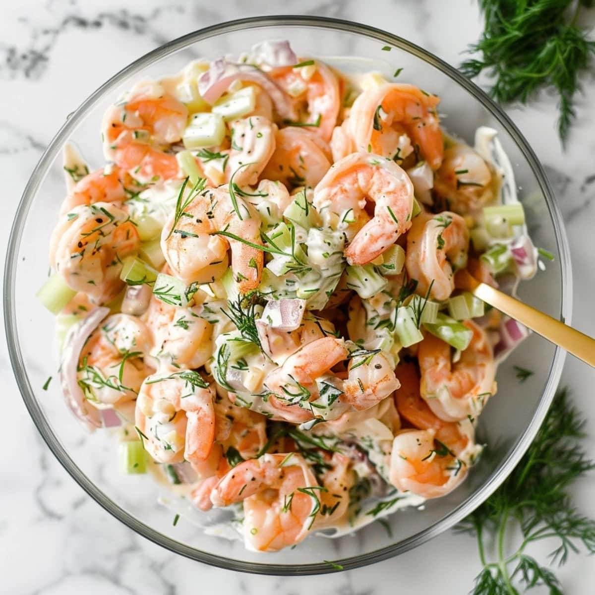 Shrimp in a glass bowl with mayonnaise dressing, red onion and celery with dill.