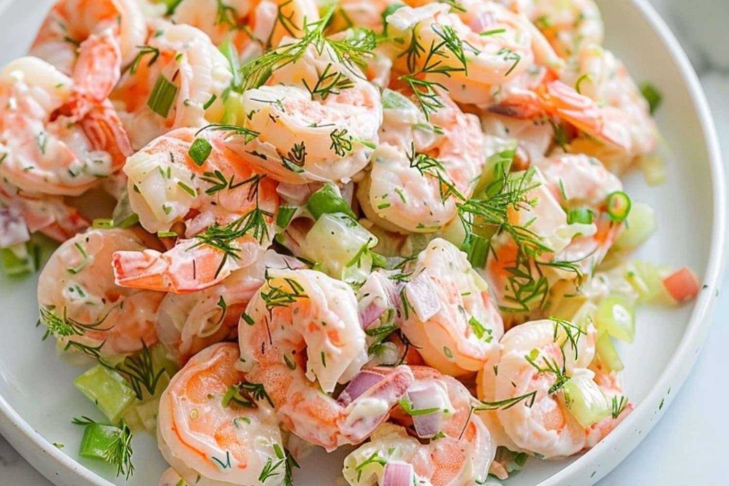 Shrimp salad with mayonnaise dressing, celery, dill and onions served on a white plate.