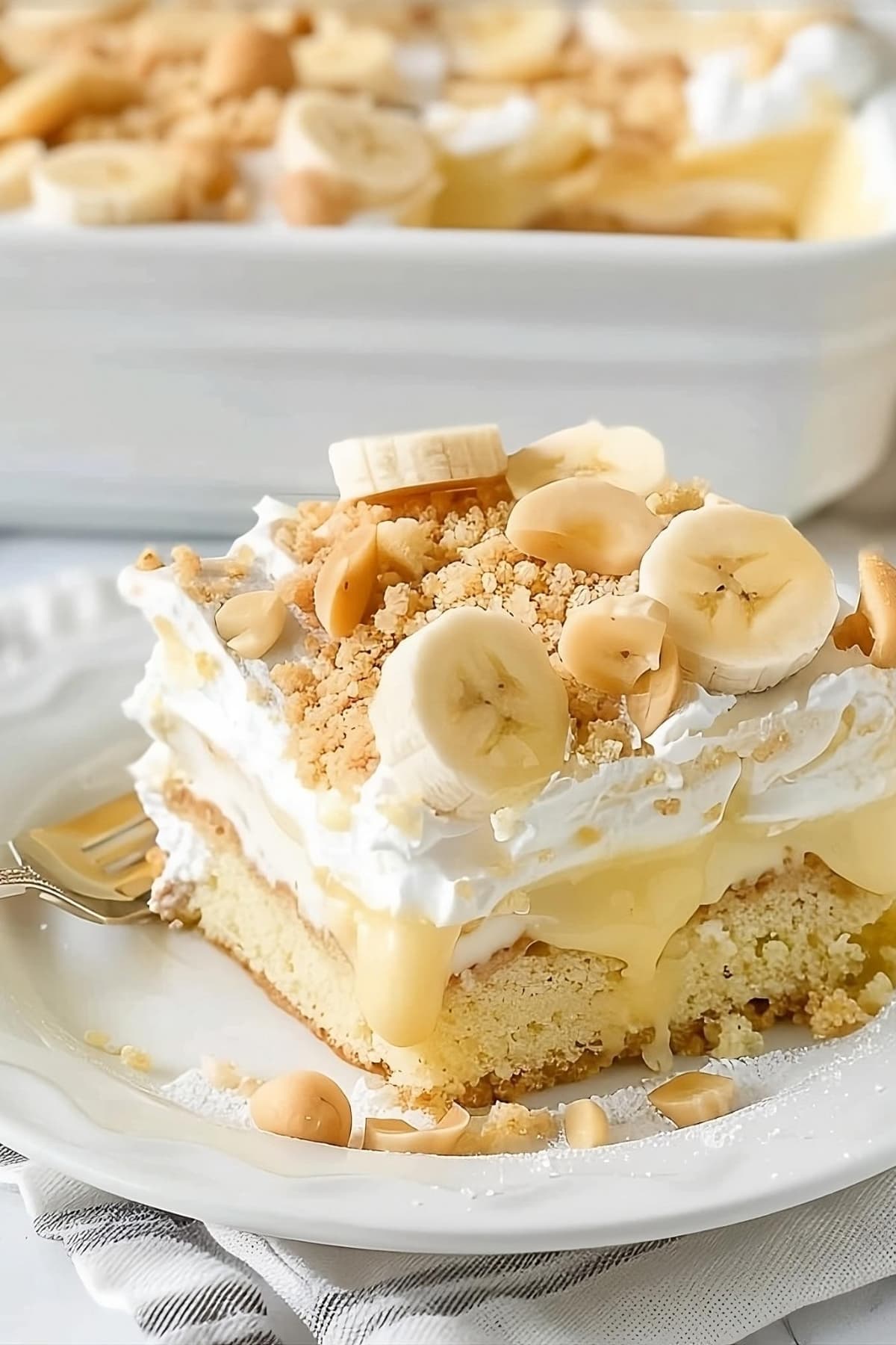 Banana pudding cake topped with whipped cream and crush wafers and sliced bananas.