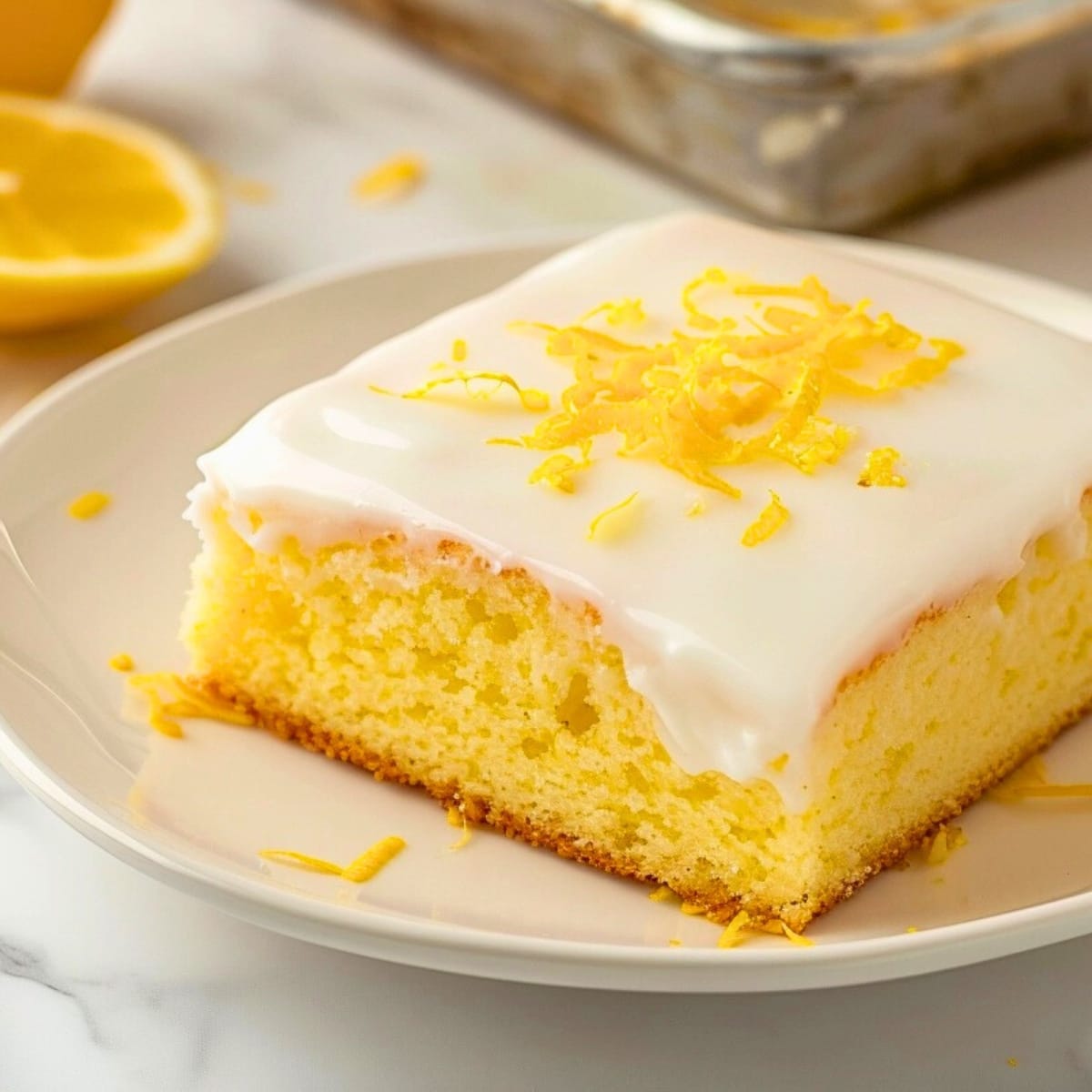 A slice of lemon sheet cake with sugar glaze garnished with lemon zest.