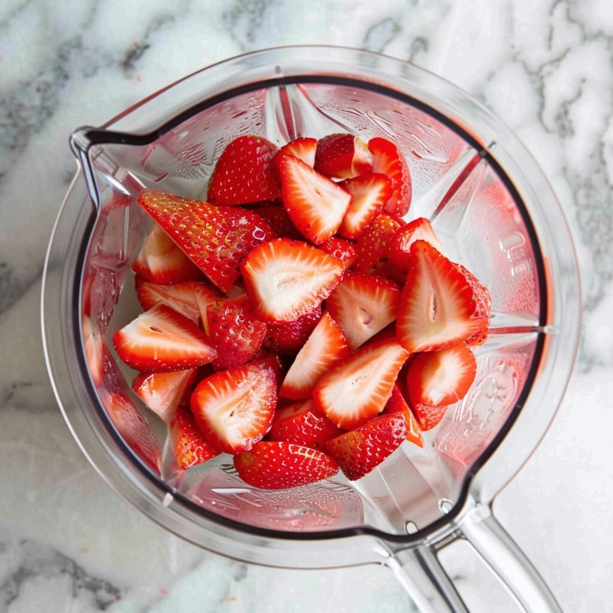 Homemade fresh sliced strawberries in a blender on a white marble table