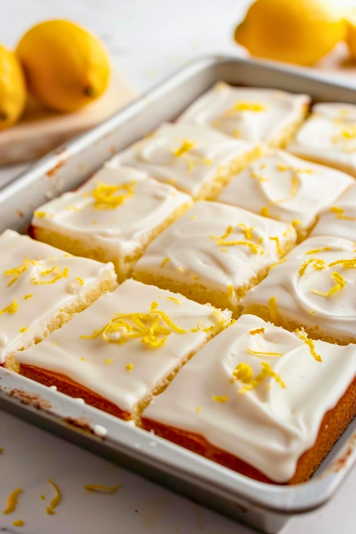 Sliced lemon sheet cake in a baking tray with lemon glaze and lemon zest.