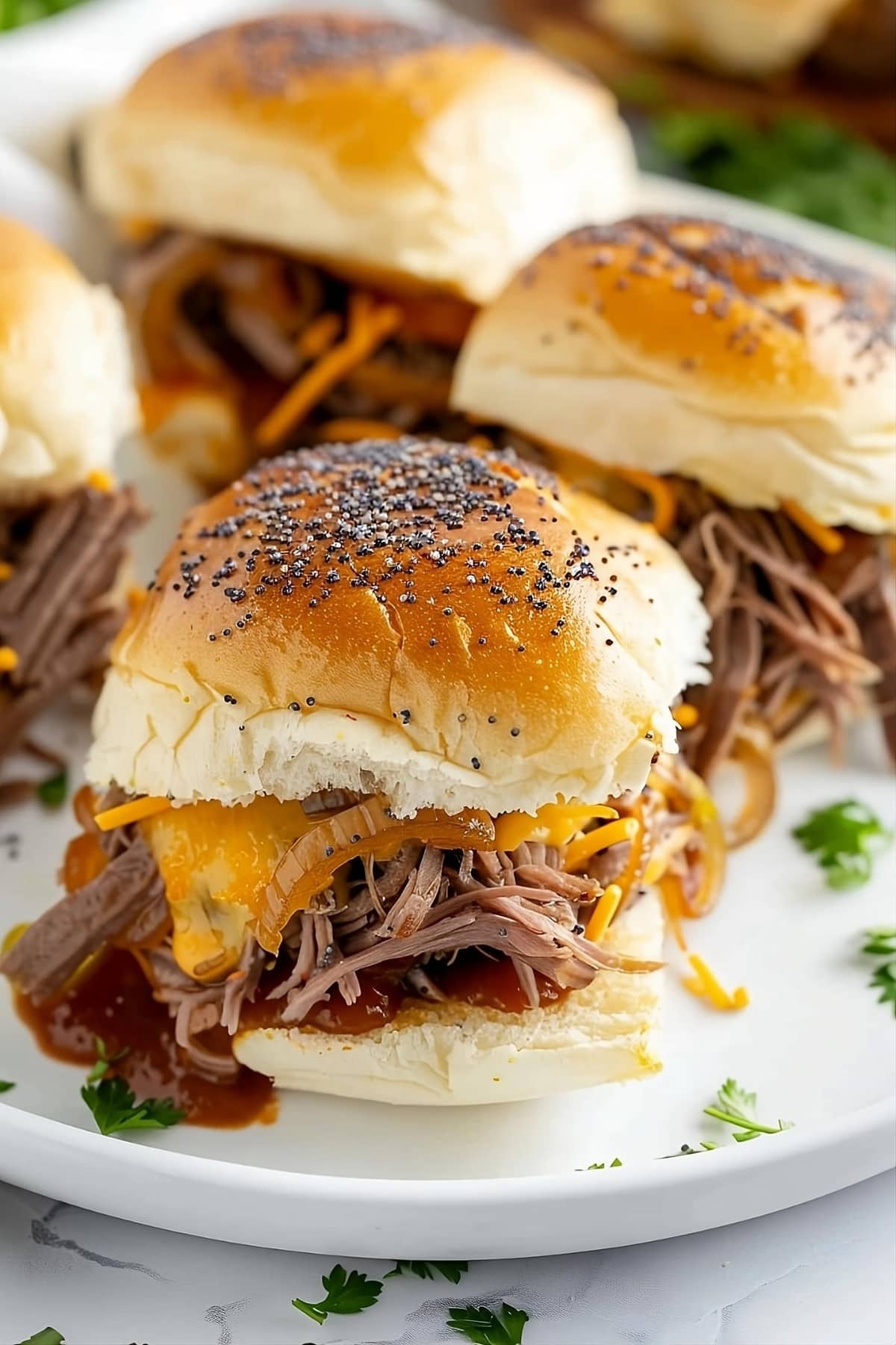 Beef and cheese sliders with poppy seeds on top served on a white plate.