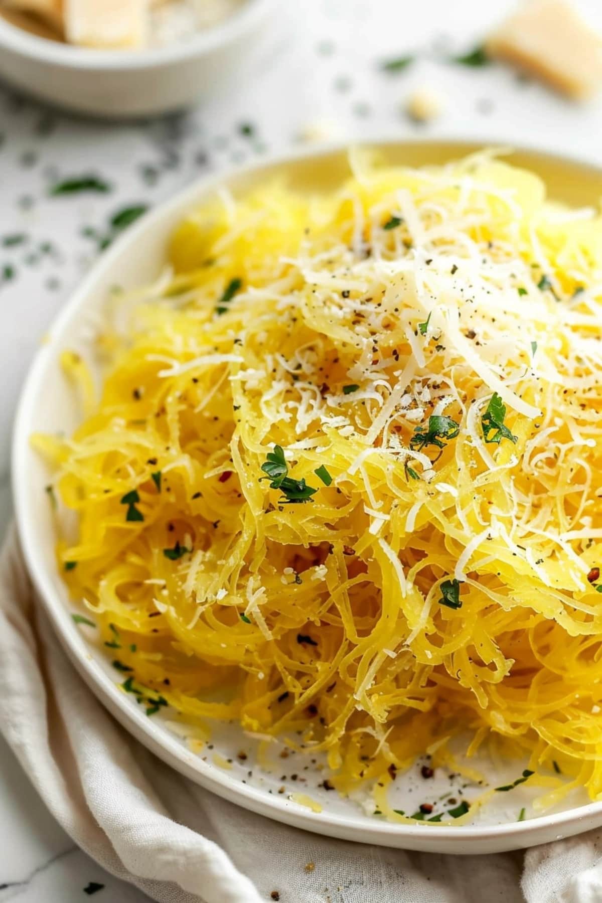 Spaghetti squash with parmesan cheese and seasoning on a white plate.
