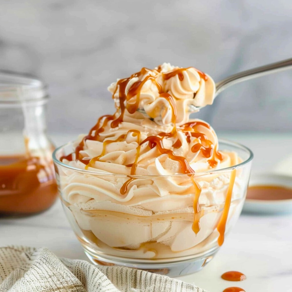 Spoon scooping salted caramel whipped cream on a glass bowl.