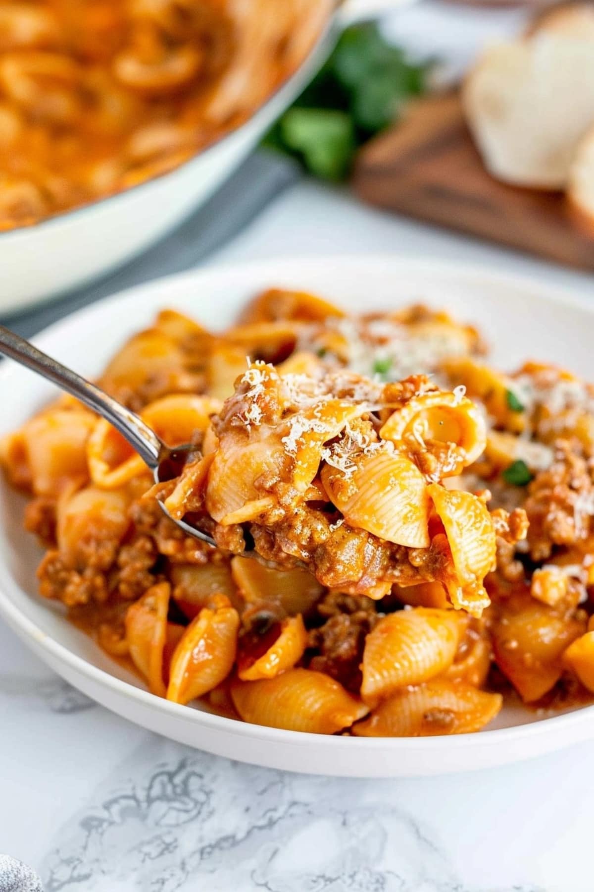Spoon scooping beef and shells in cheesy tomato sauce with ground beef and cheese.