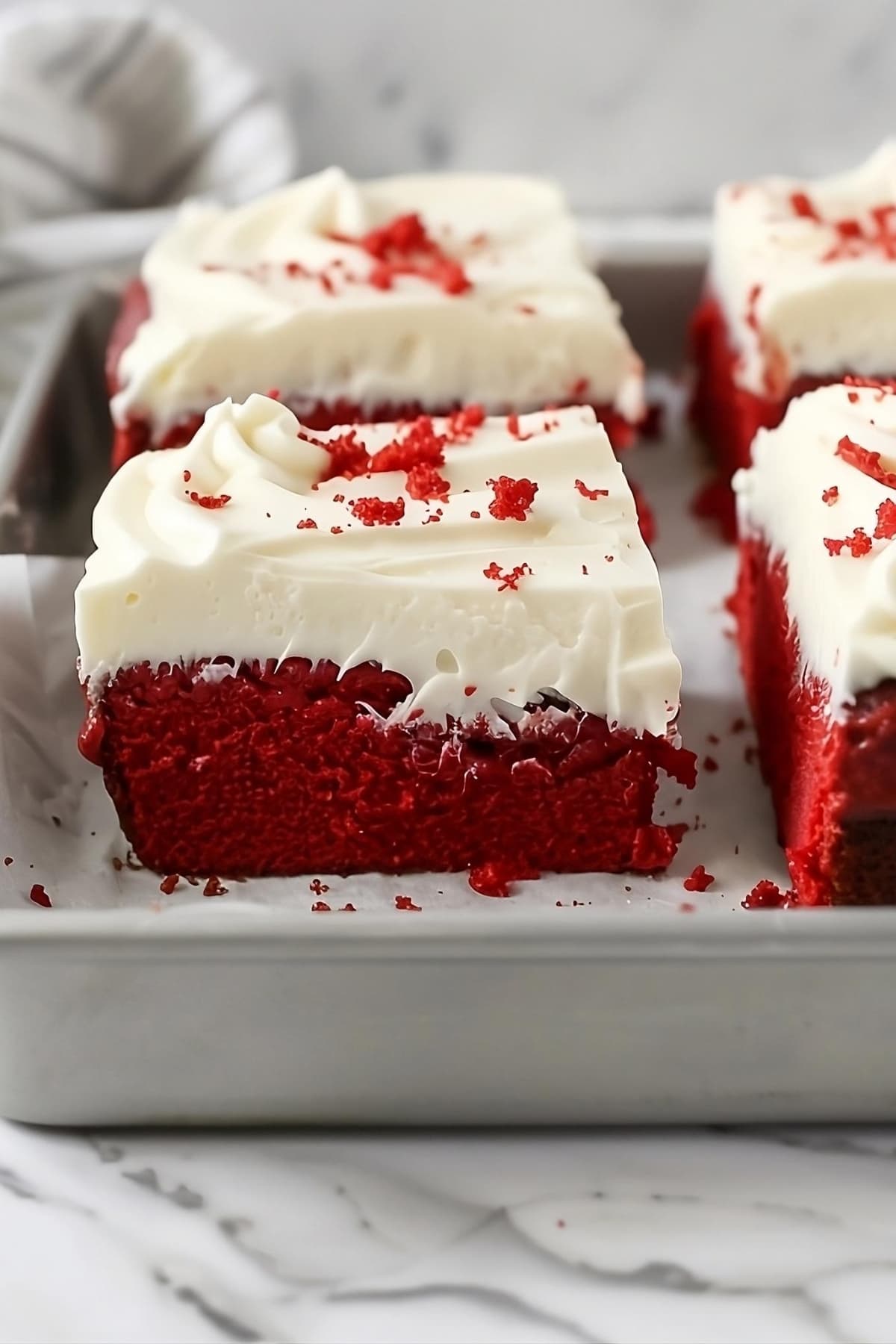 Square slices of red velvet sheet cake in a baking pan.