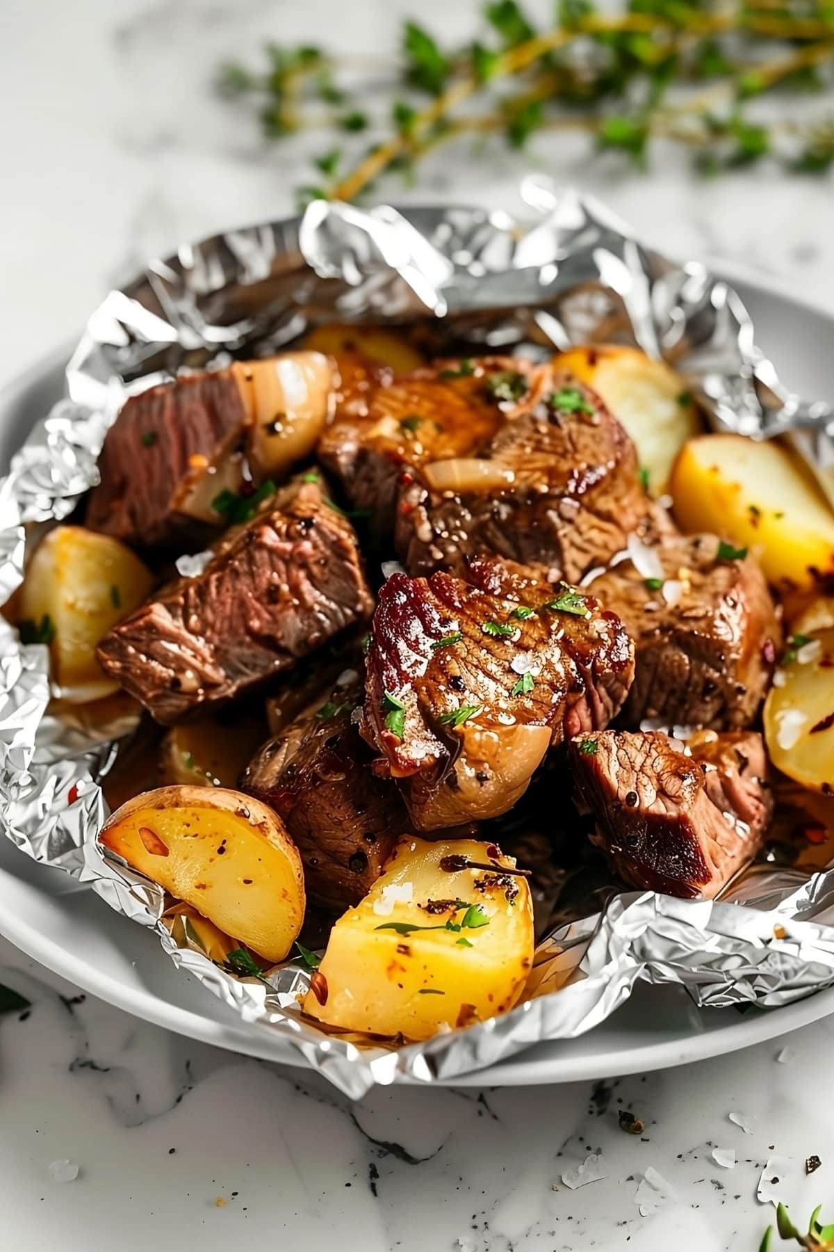 Grilled steak and baby potatoes inside an aluminum foil served on a white plate.