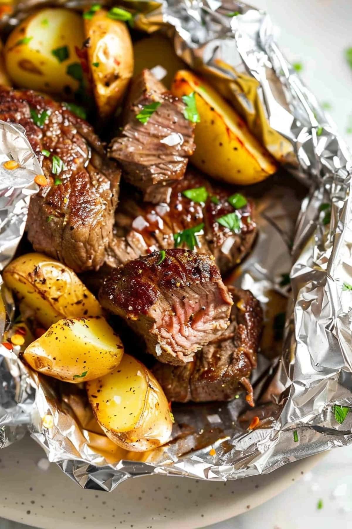 Cube sliced steak and baby potatoes grilled while inside an aluminum foil packet.