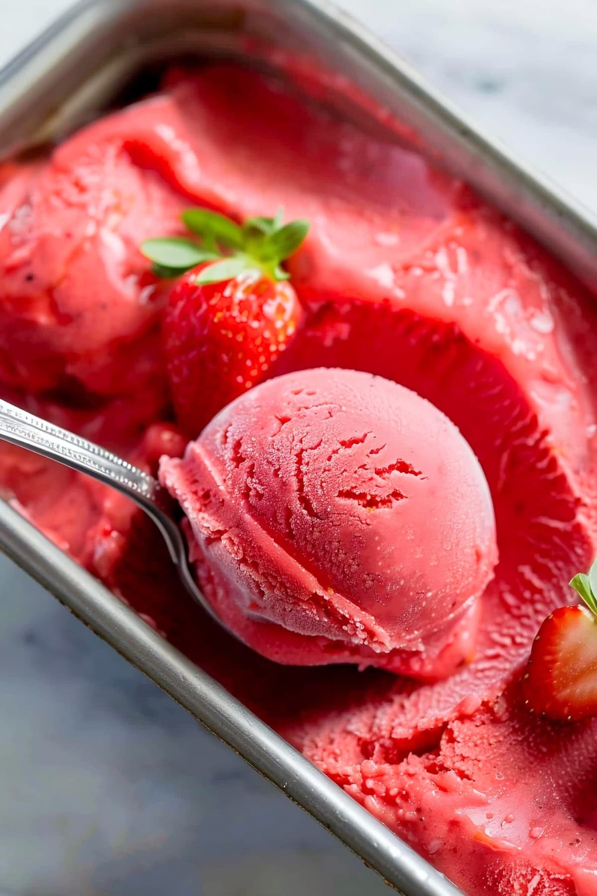 A scoop of strawberry sorbet in a stainless container