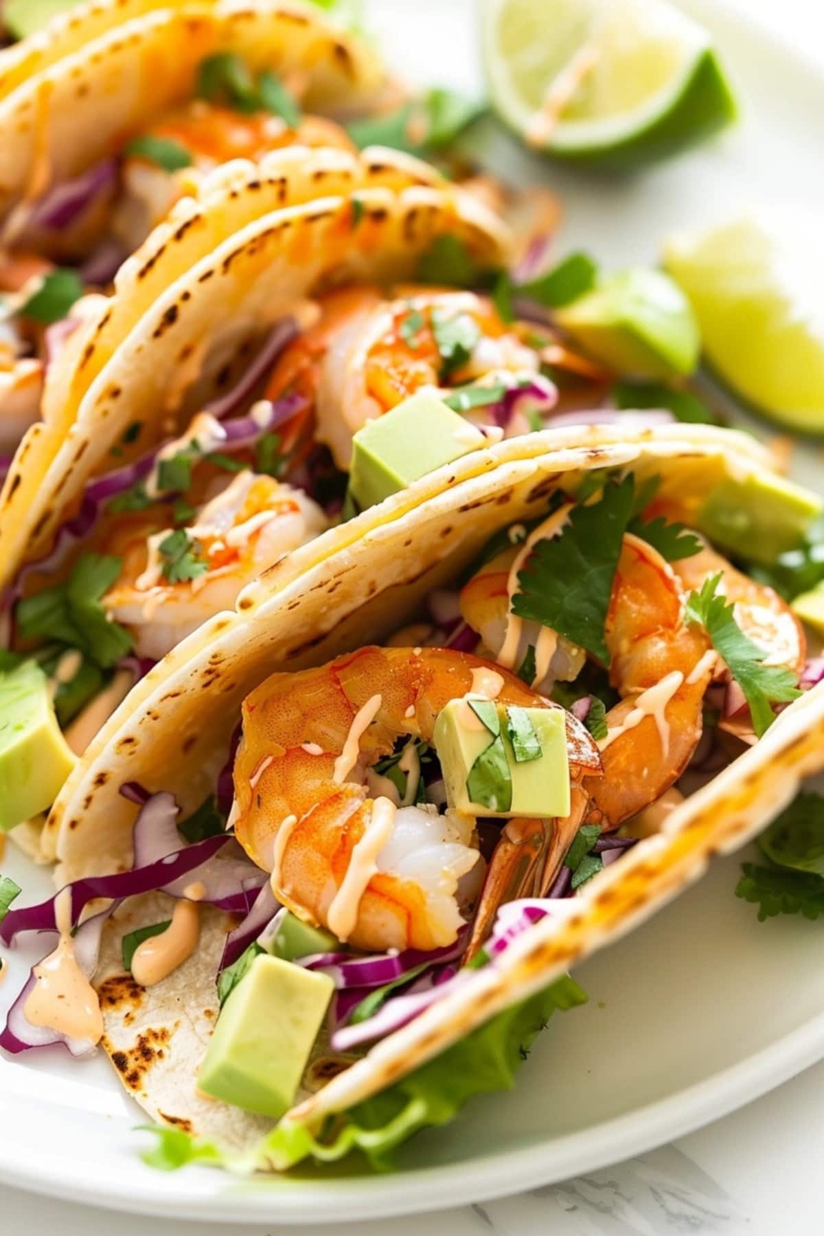 Taco shrimp on a white plate with shrimp, avocado, shredded red cabbage, onion, salsa drizzled with dressing.