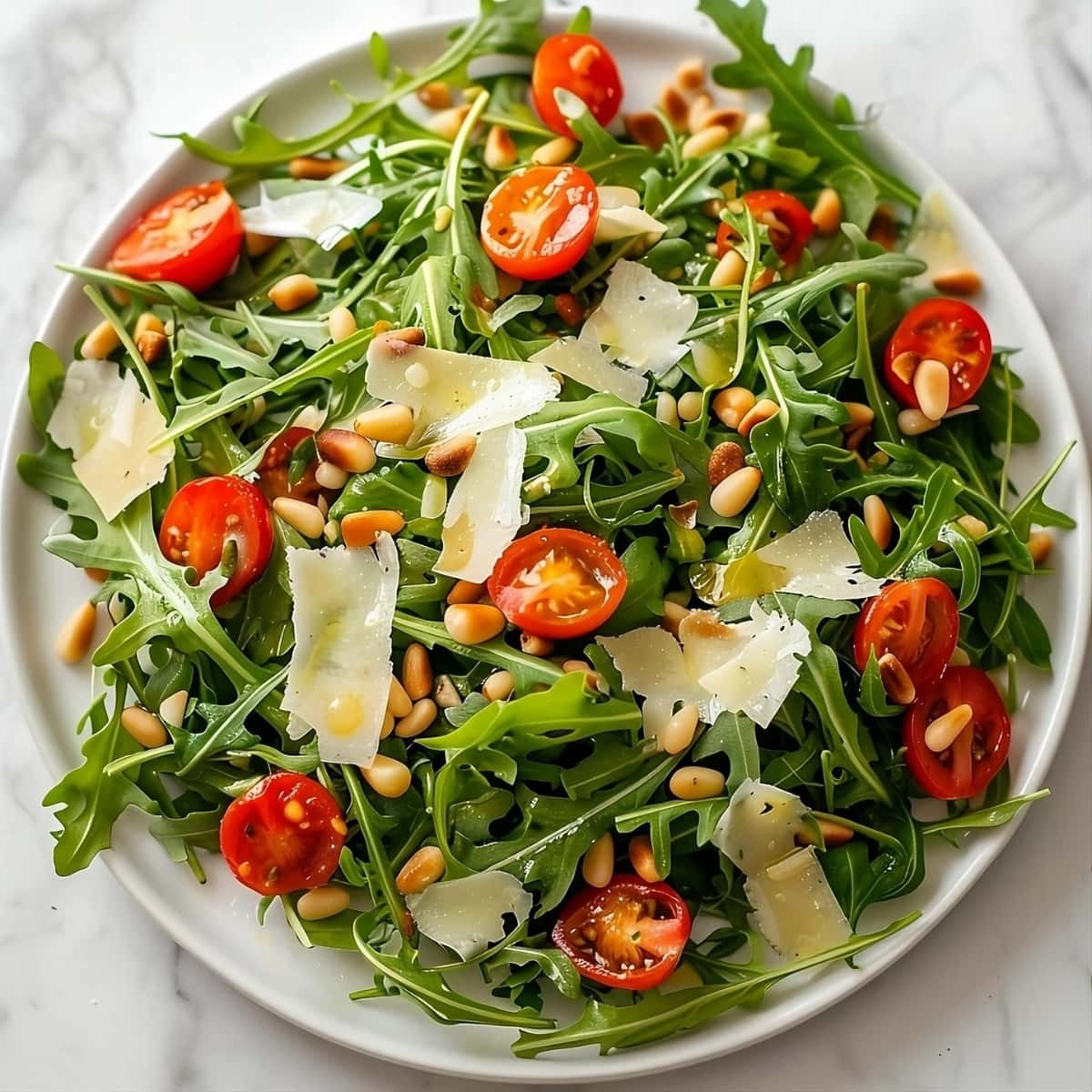Arugula salad with cherry tomatoes, arugula and roasted pine nuts drizzled with lemon dressing garnished with shaved parmesan cheese.