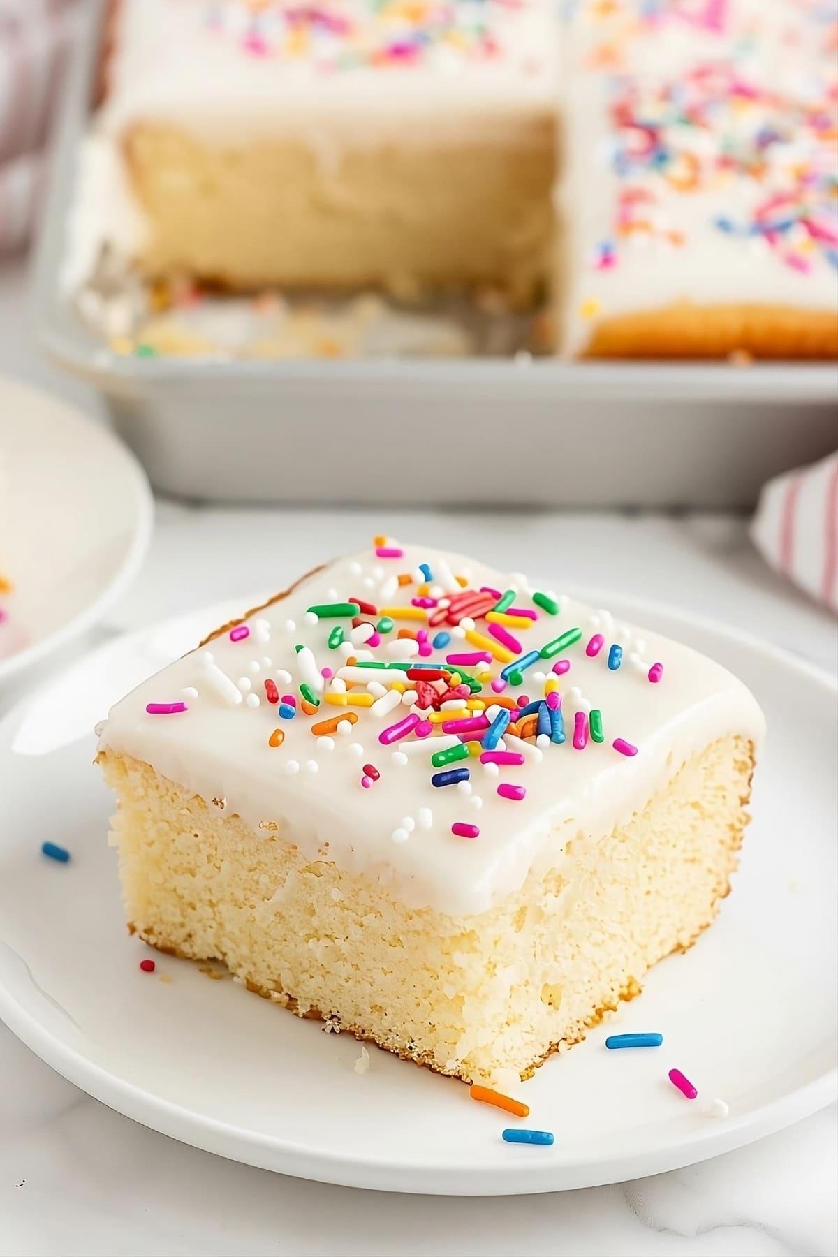 A slice of vanilla sheet cake in a white plate with sprinkles.