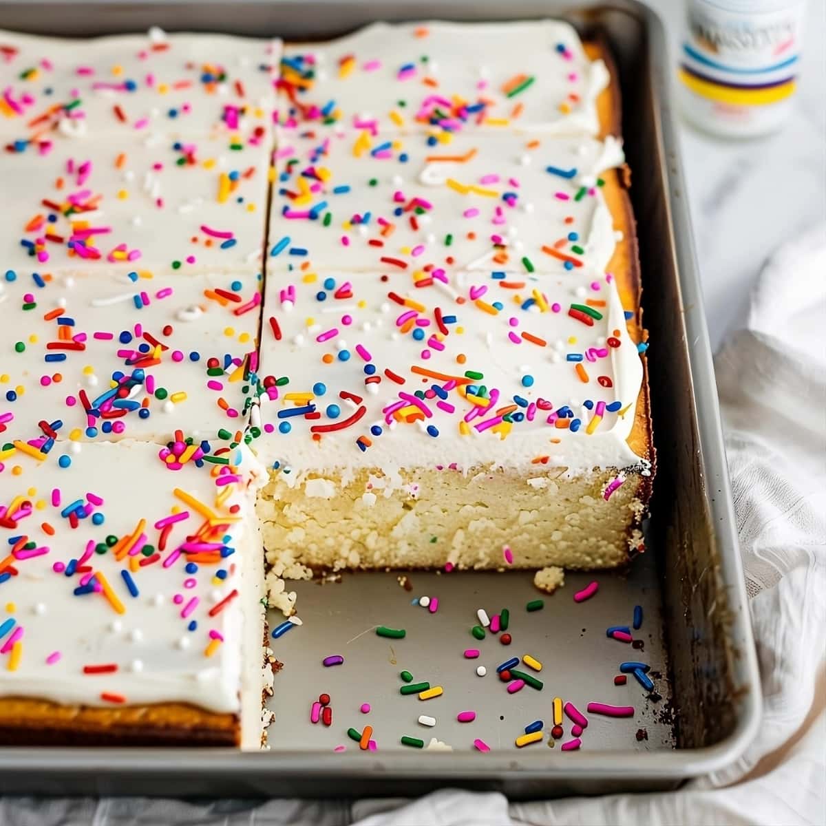 Sliced vanilla sheet cake, portion missing in a baking sheet.