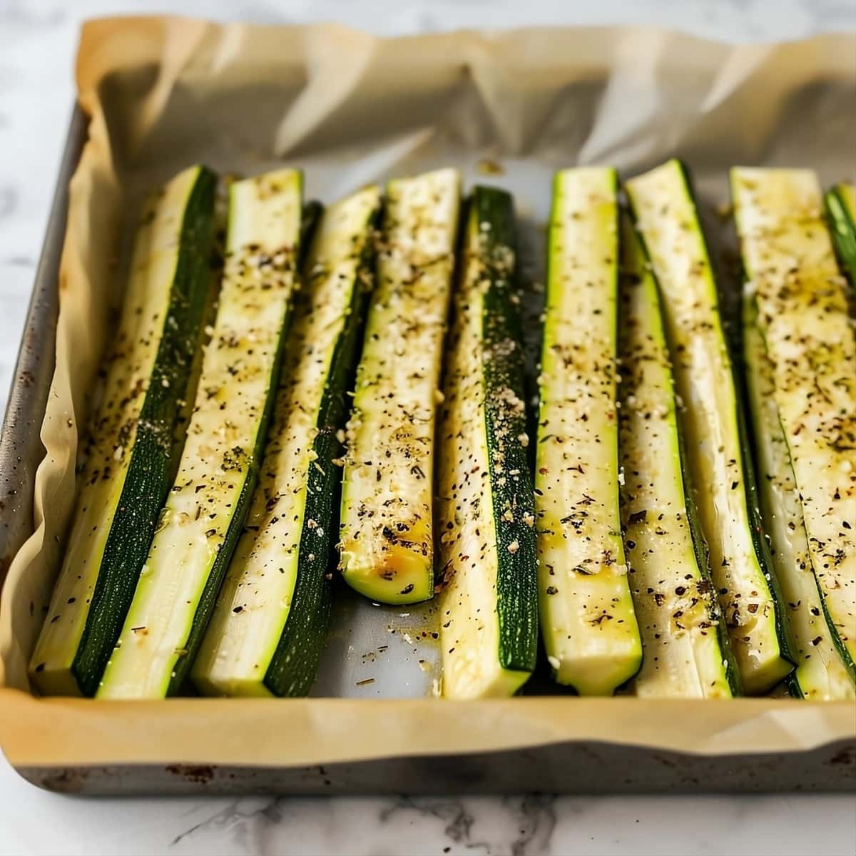 Seasoned zucchini slices in a baking sheet with parchment paper.