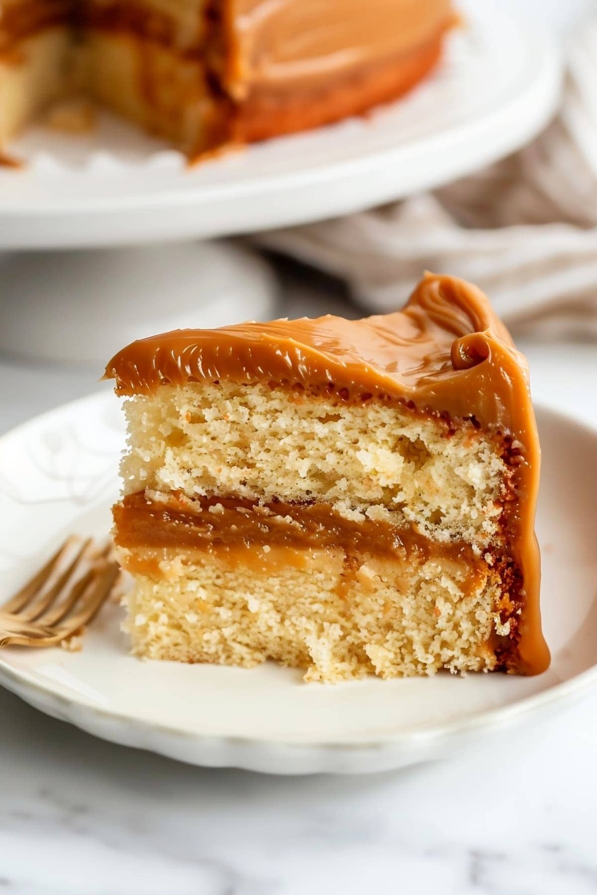A slice of cake with caramel frosting on a white plate ready to be enjoyed