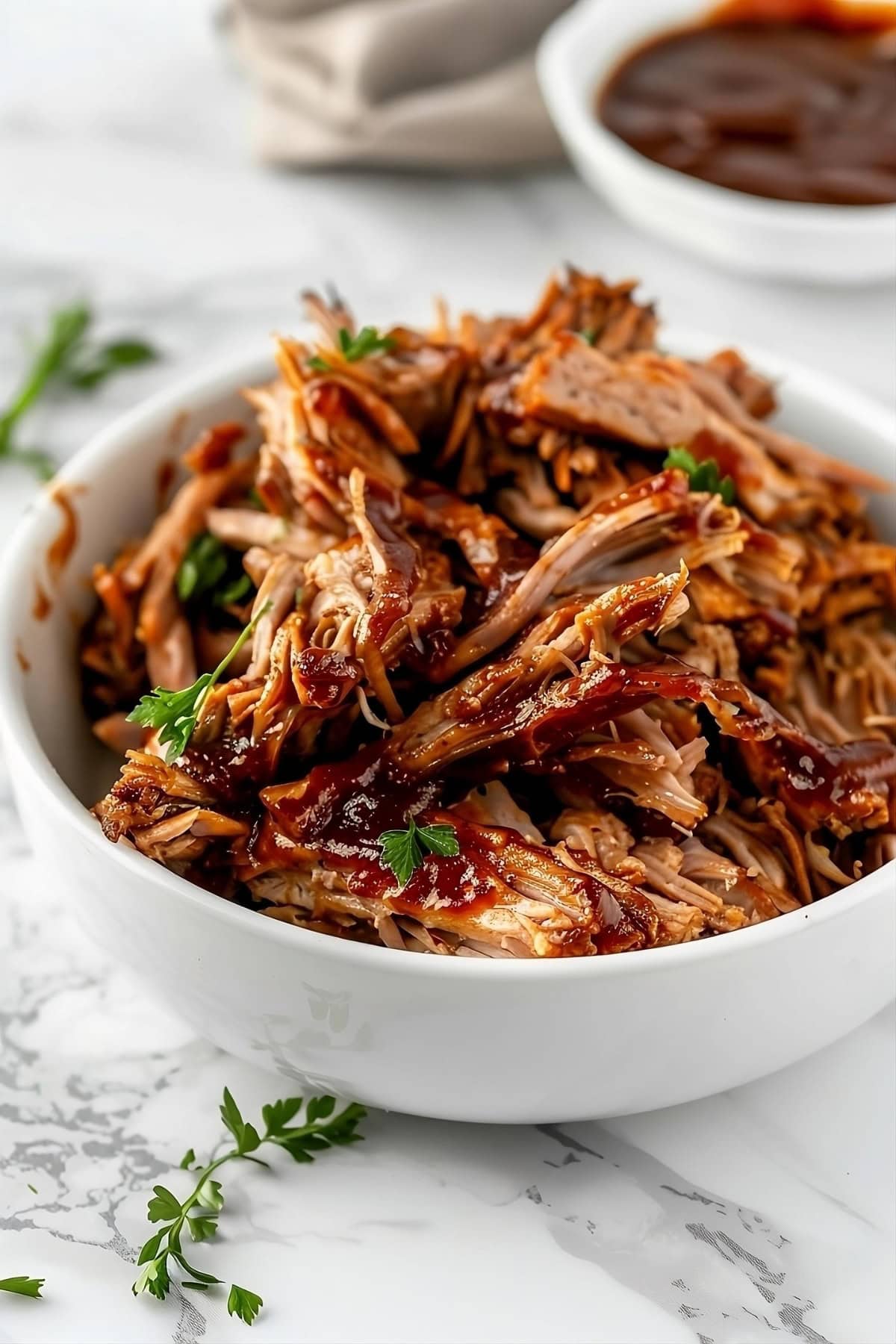Barbeque sauce flavored pulled pork in a white bowl.