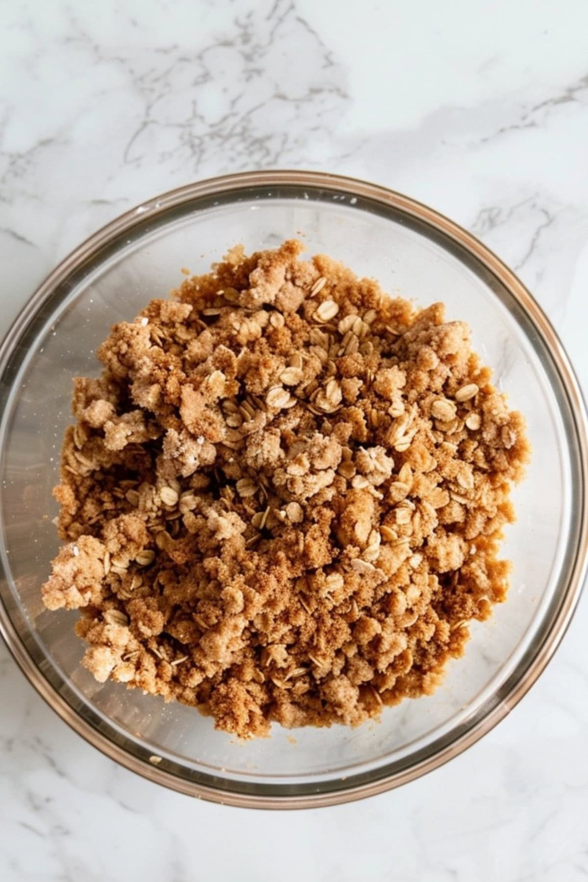 Apple crisp topping made with mixed oats, flour, brown sugar, cinnamon, and salt and butter mixed together to make a coarse crumbs as apple crisp toppings sitting on a white marble table.