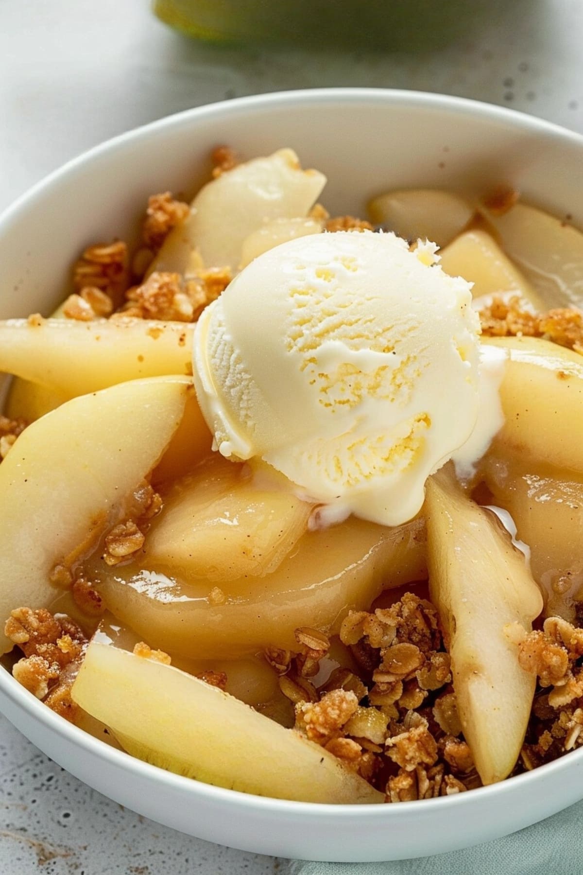 Baked pear crisp in a white bowl garnished with vanilla ice cream.