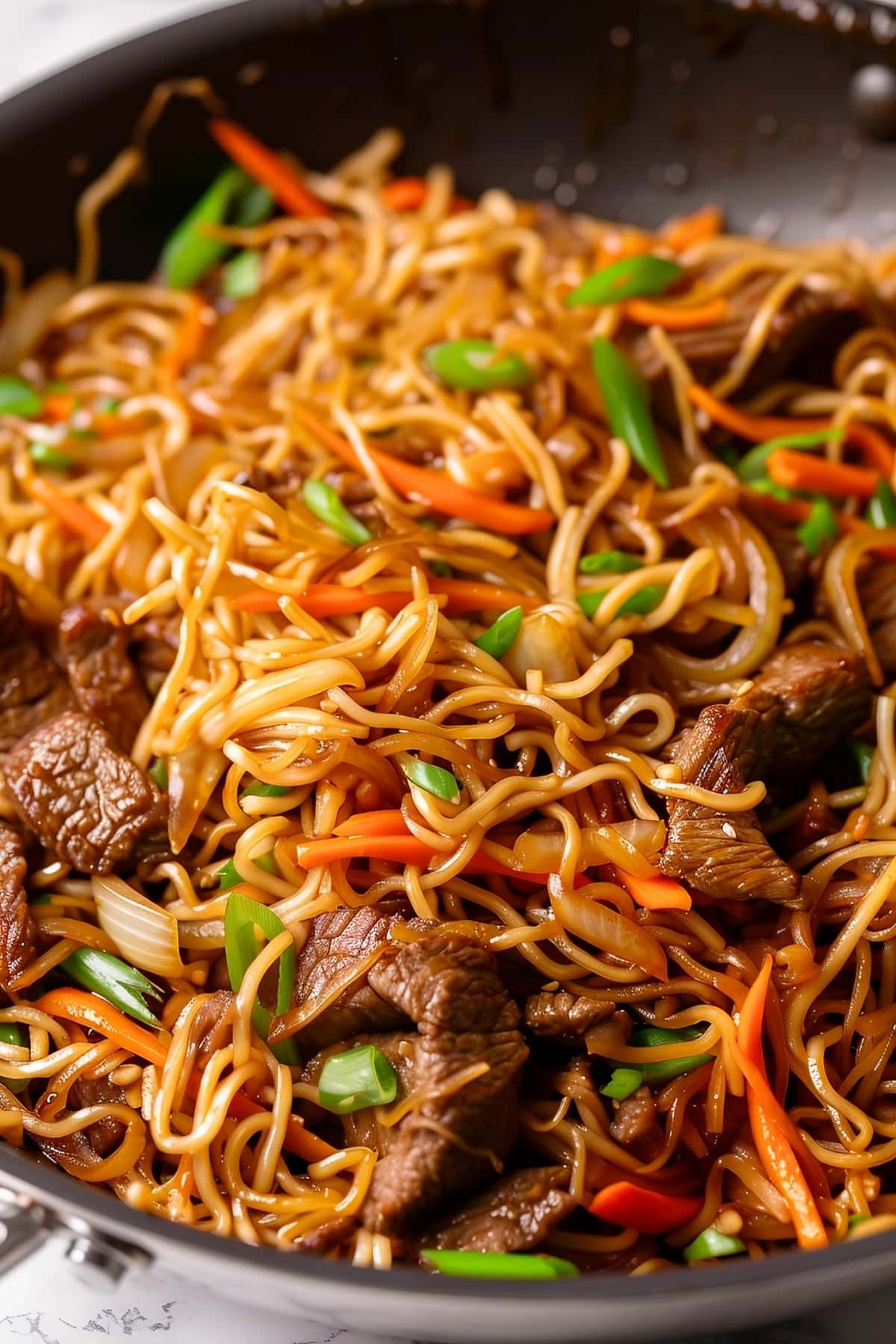 Beef chow mein noodles with tender flank steak and colorful vegetables in a black skillet