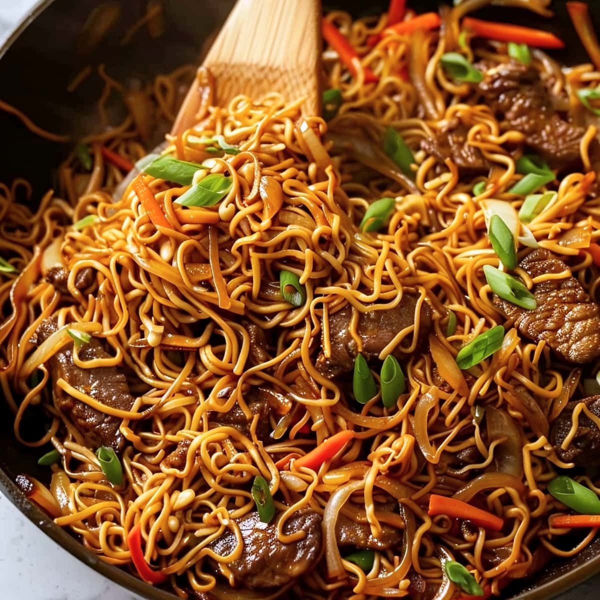 Beef chow mein noodles in a black skillet with stir-fried vegetables and beef