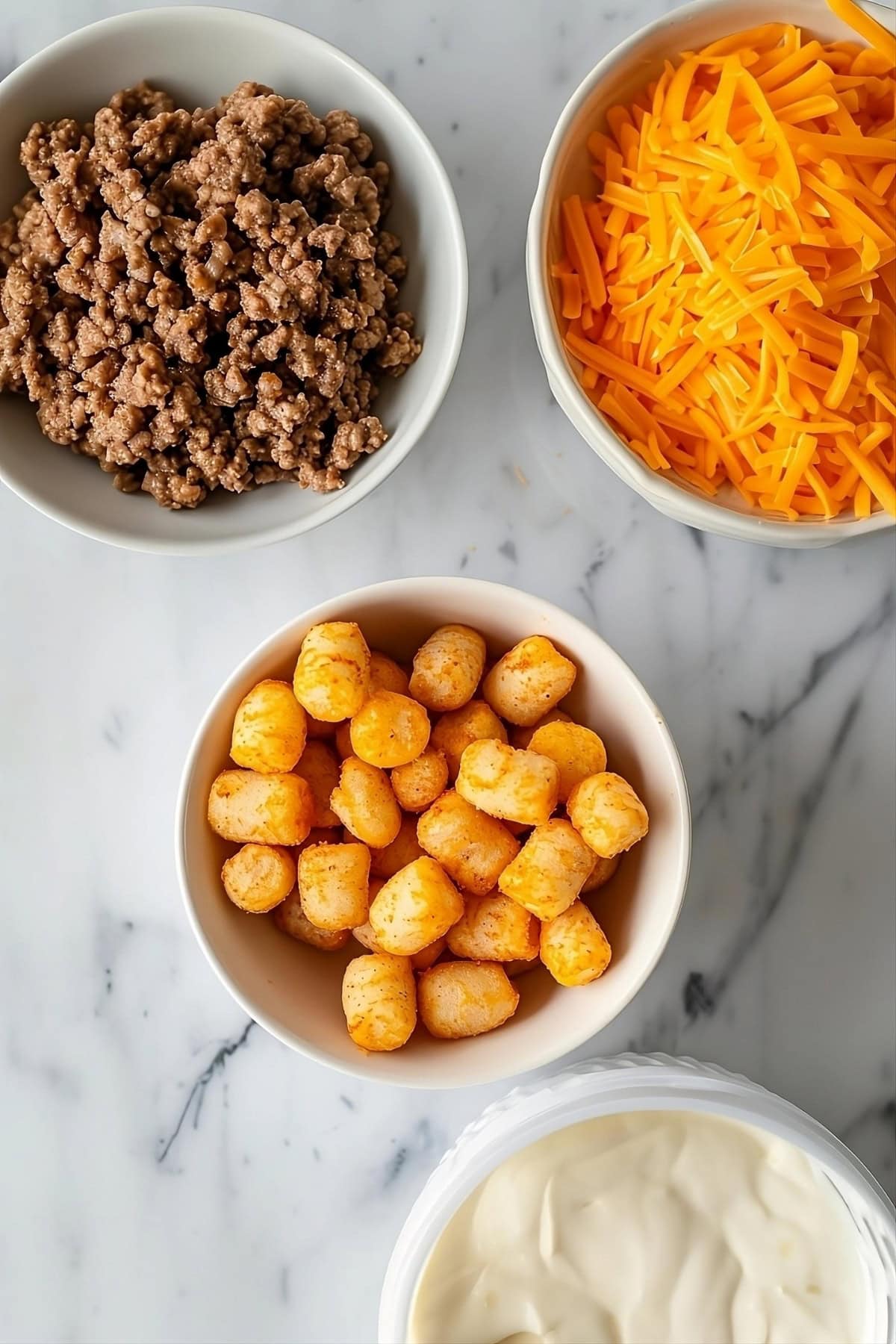 Ground beef, cheddar cheese, tater tots and dressing in bowl.