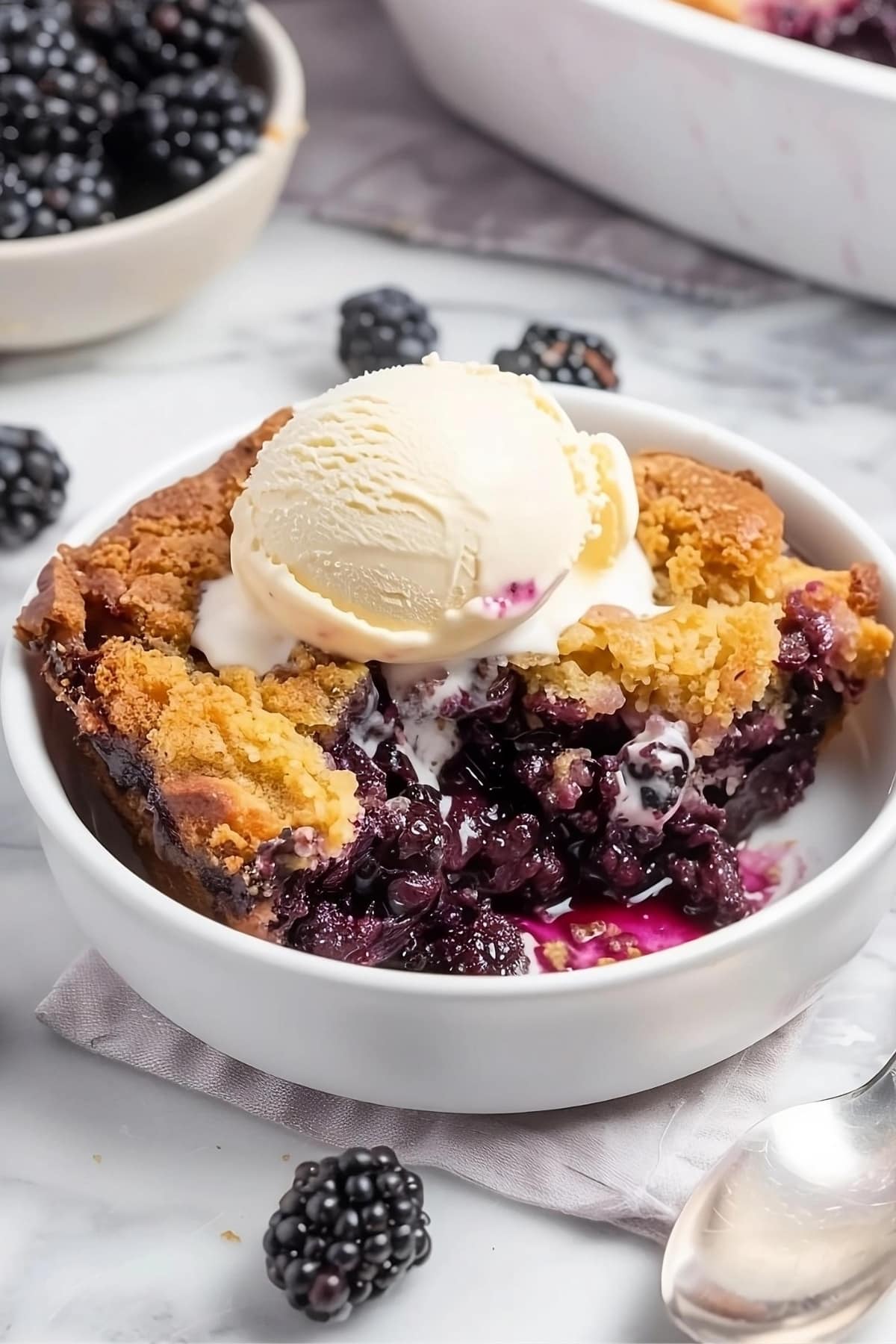 Blackberry dump cake in a white bowl garnished with a scoop of vanilla ice cream.
