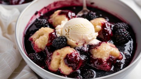 Blackberry dumplings in a white bowl topped with vanilla ice cream.