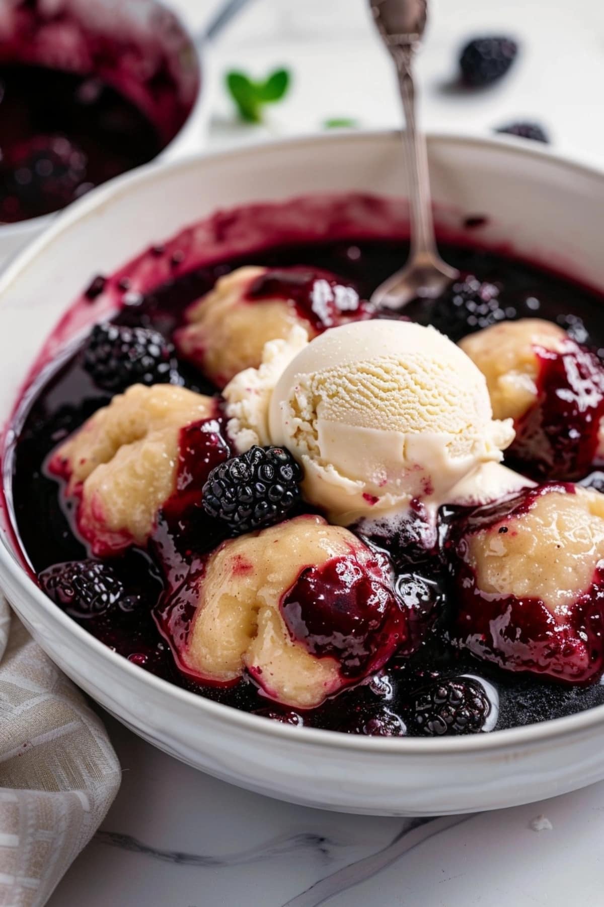Blackberry dumpling with jamlike sauce served in a white bowl topped with vanilla ice cream.