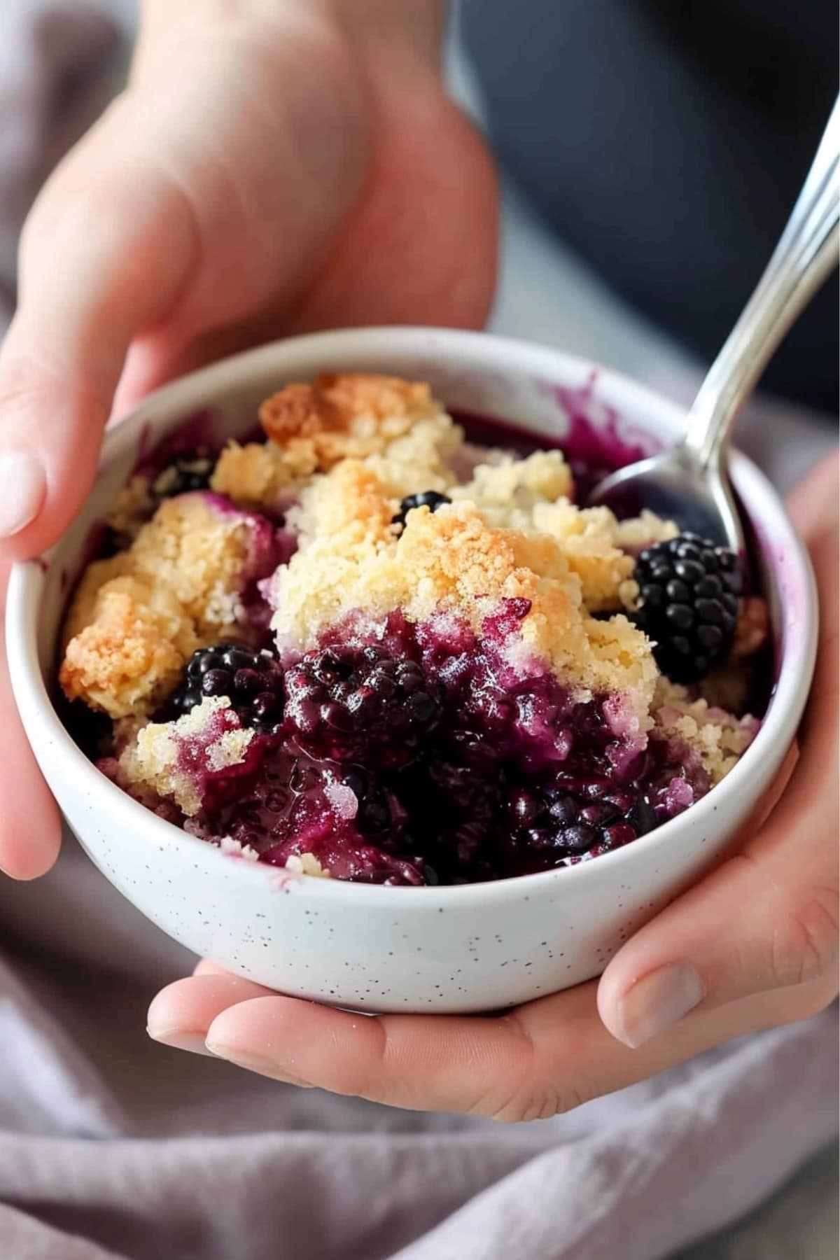 Blackberry dump cake in a bowl with spoon held with two hands.