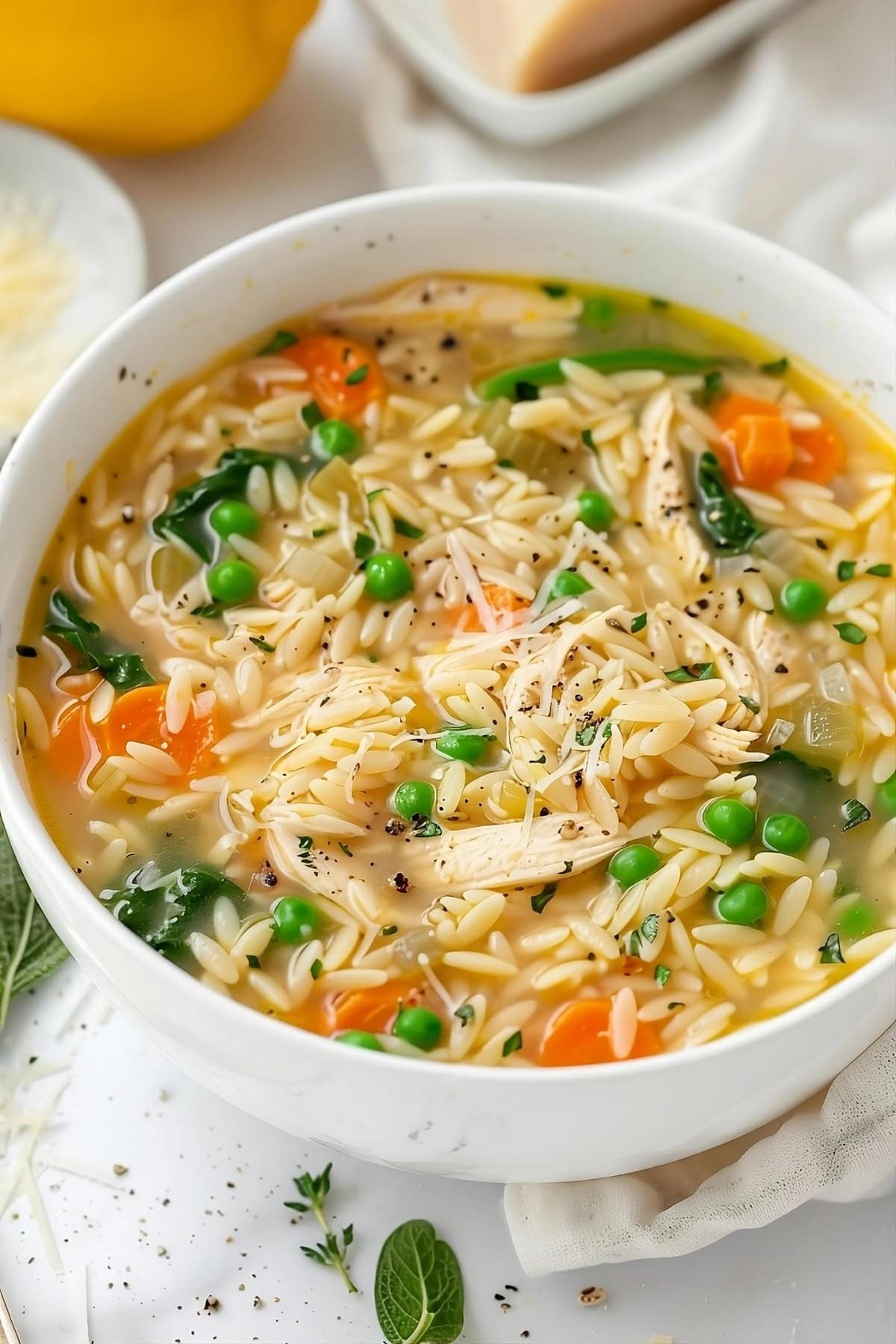 Chicken soup with orzo pasta, carrots, green peas and spinach served in a white bowl.