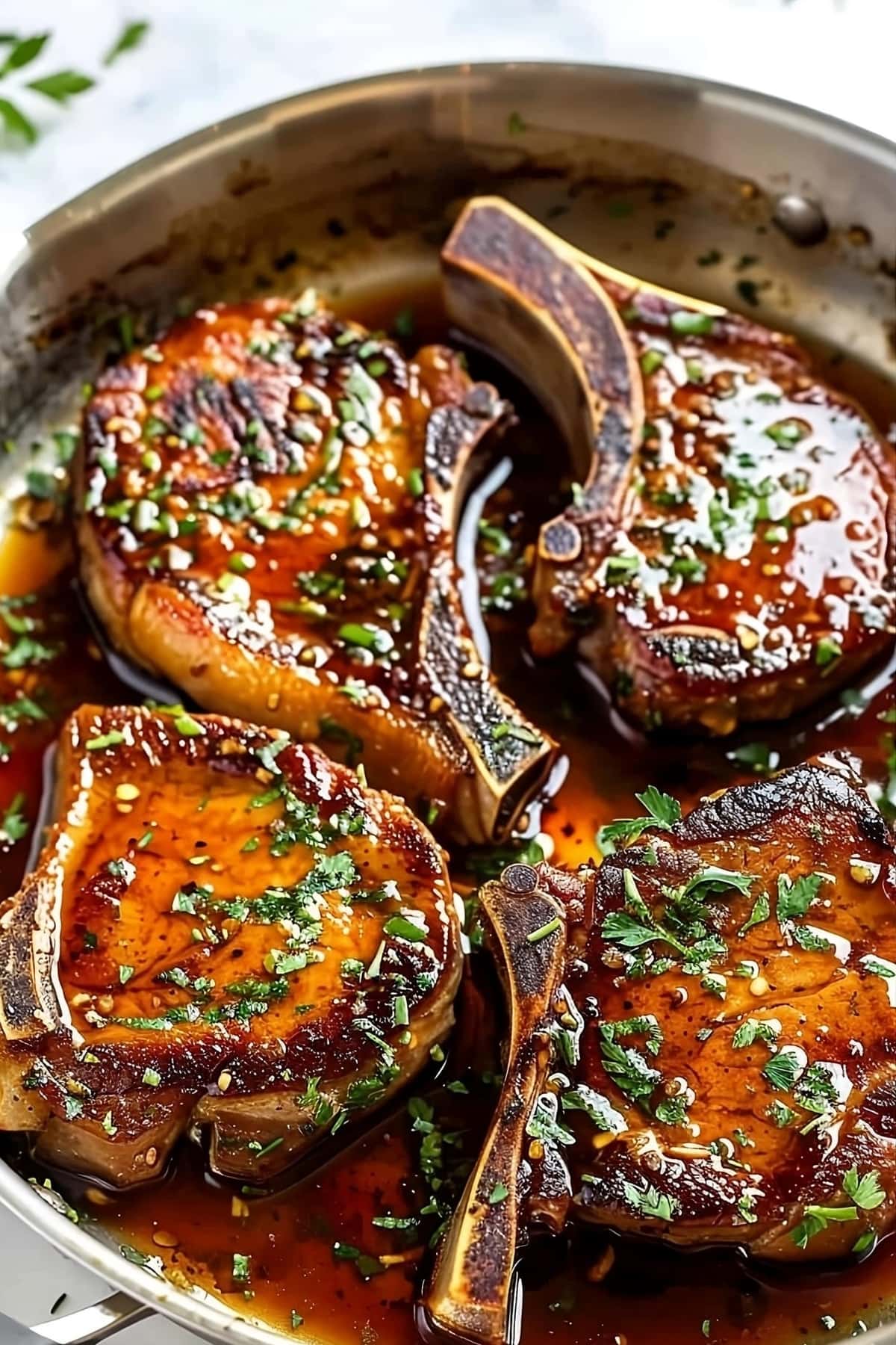 Pork chops in a skillet with glazing sauce.