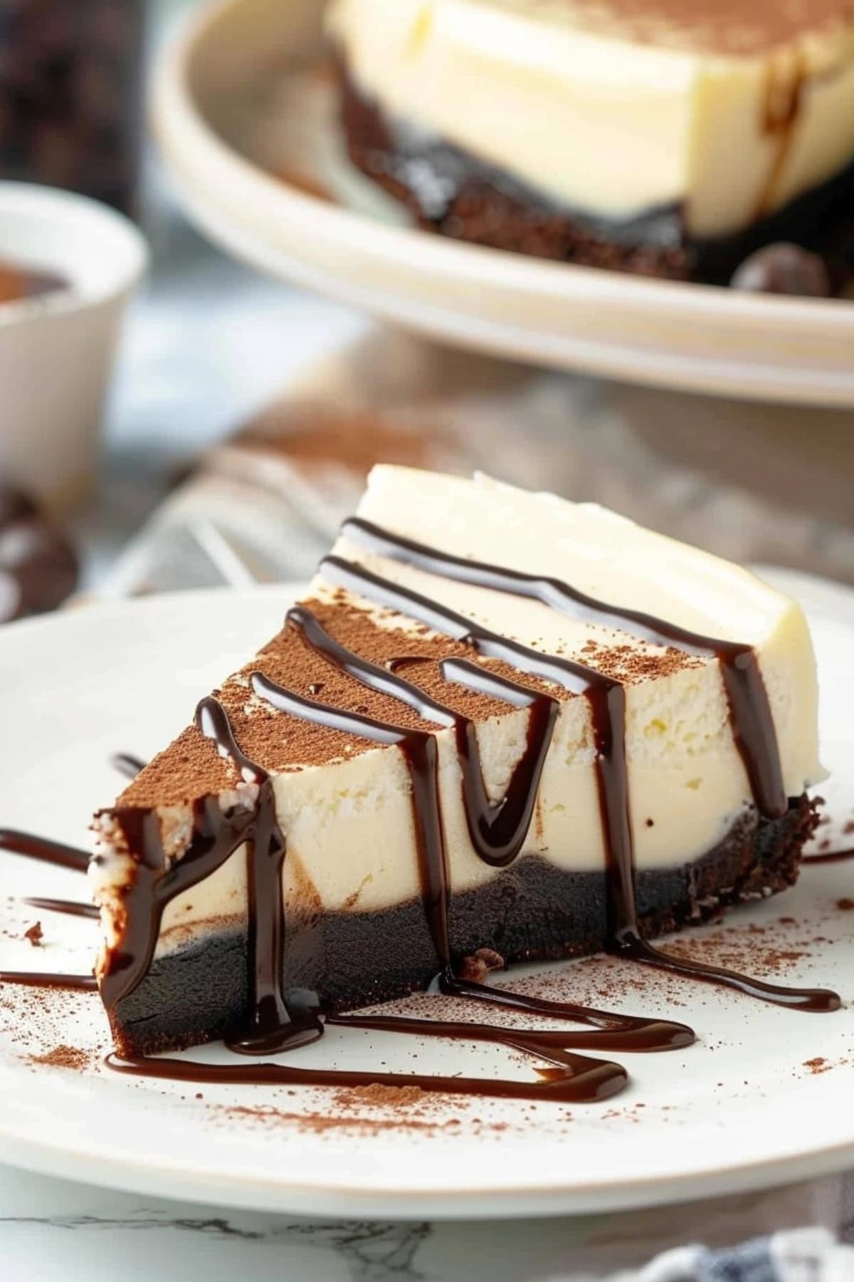Slice of creamy cheesecake with brownie base drizzled with chocolate syrup.