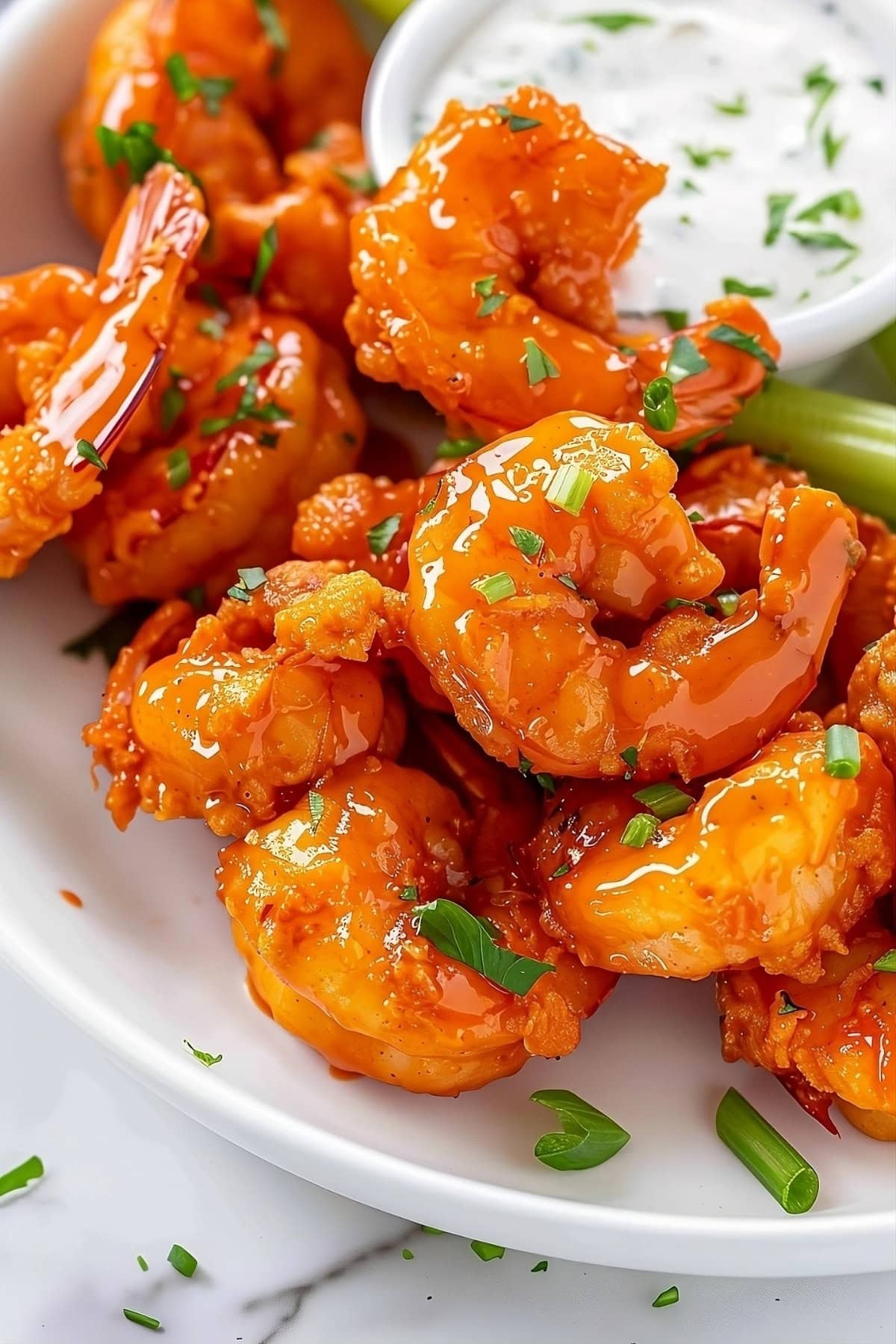 Buffalo shrimp in a white plate with celery sticks and ranch dip.