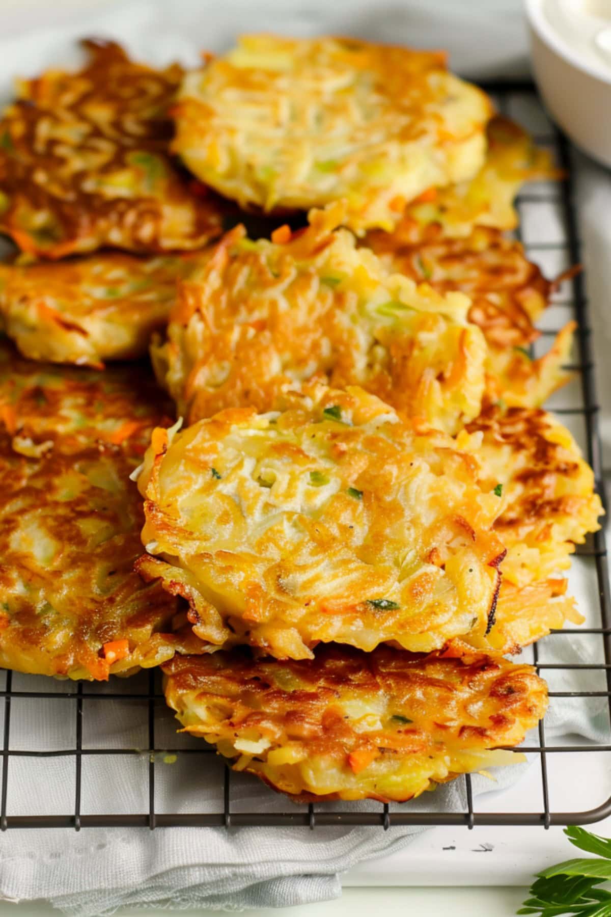 Cabbage fritters in a cooling rack with sour cream on the side on a white marble countertop