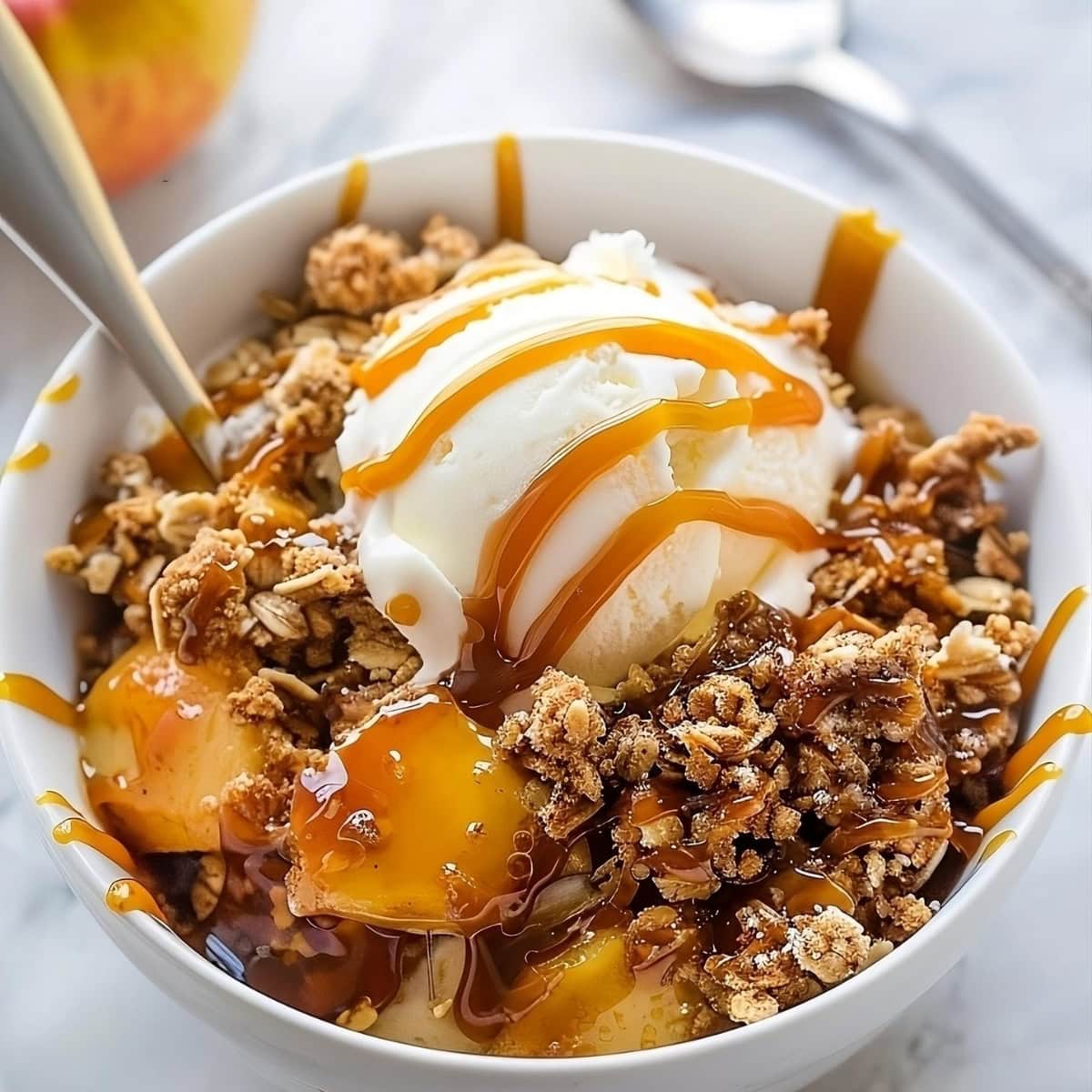 Serving of Caramel Apple Crisp in a white bowl garnished with vanilla ice cream drizzled with more caramel.