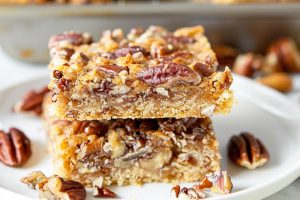 Caramel pecan bars slices stack on a white plate.