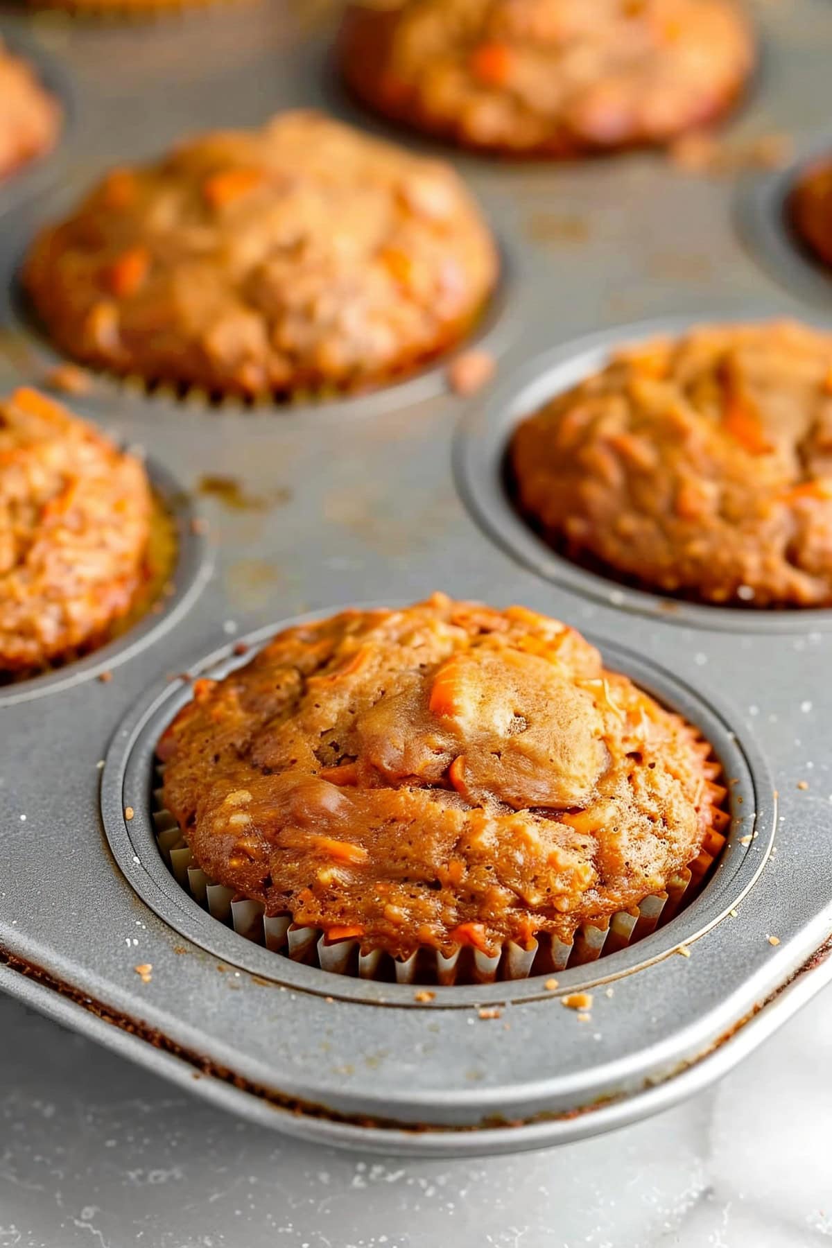 Carrot muffins in a muffin tin on a white marble table