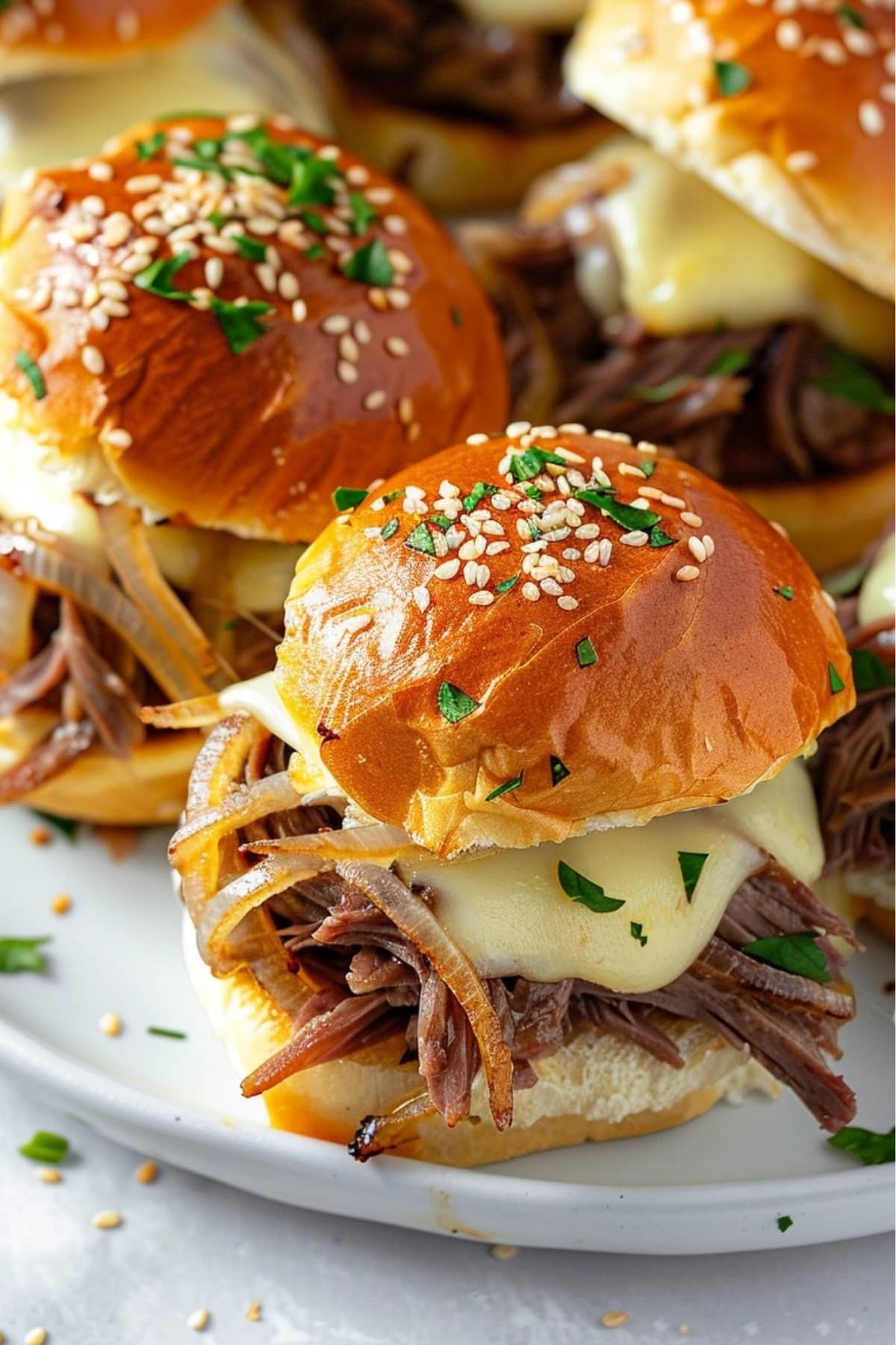 Cheesy French dip sliders on a white plate.