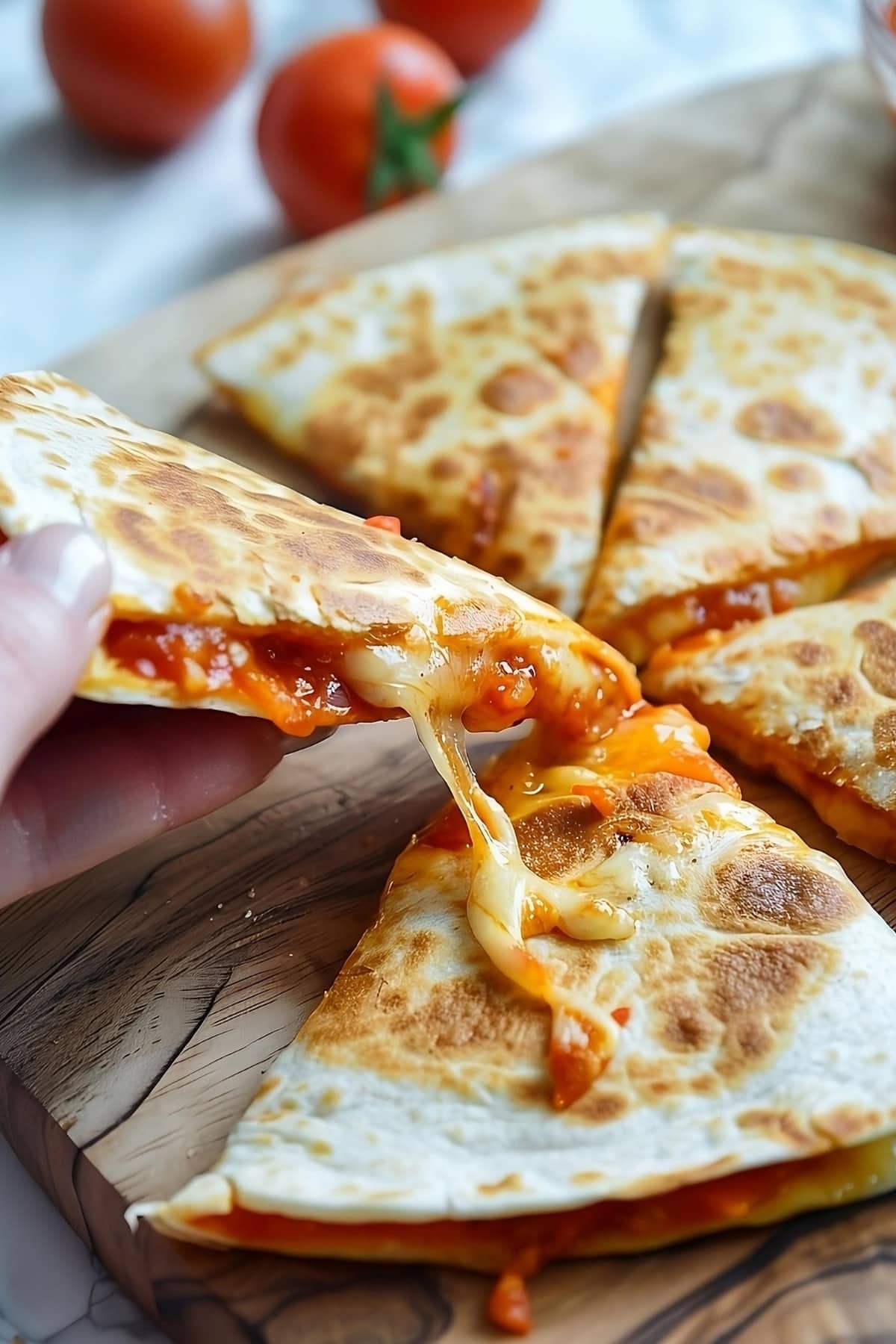 Hand lifting a slice of cheesy pizza quesadilla in a wooden board.
