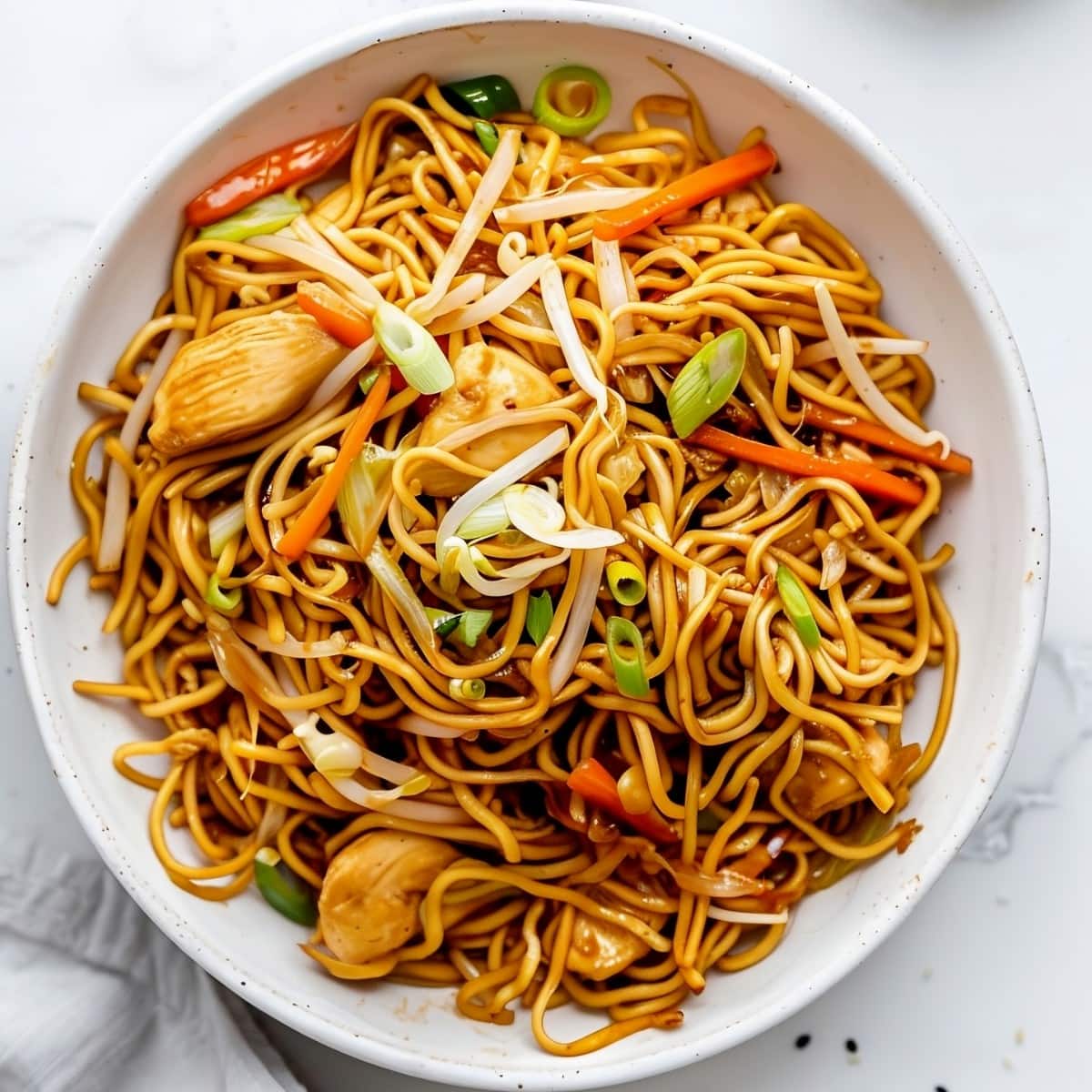 A bowl of chow mein noodles with chicken, carrots, onions and bean sprouts