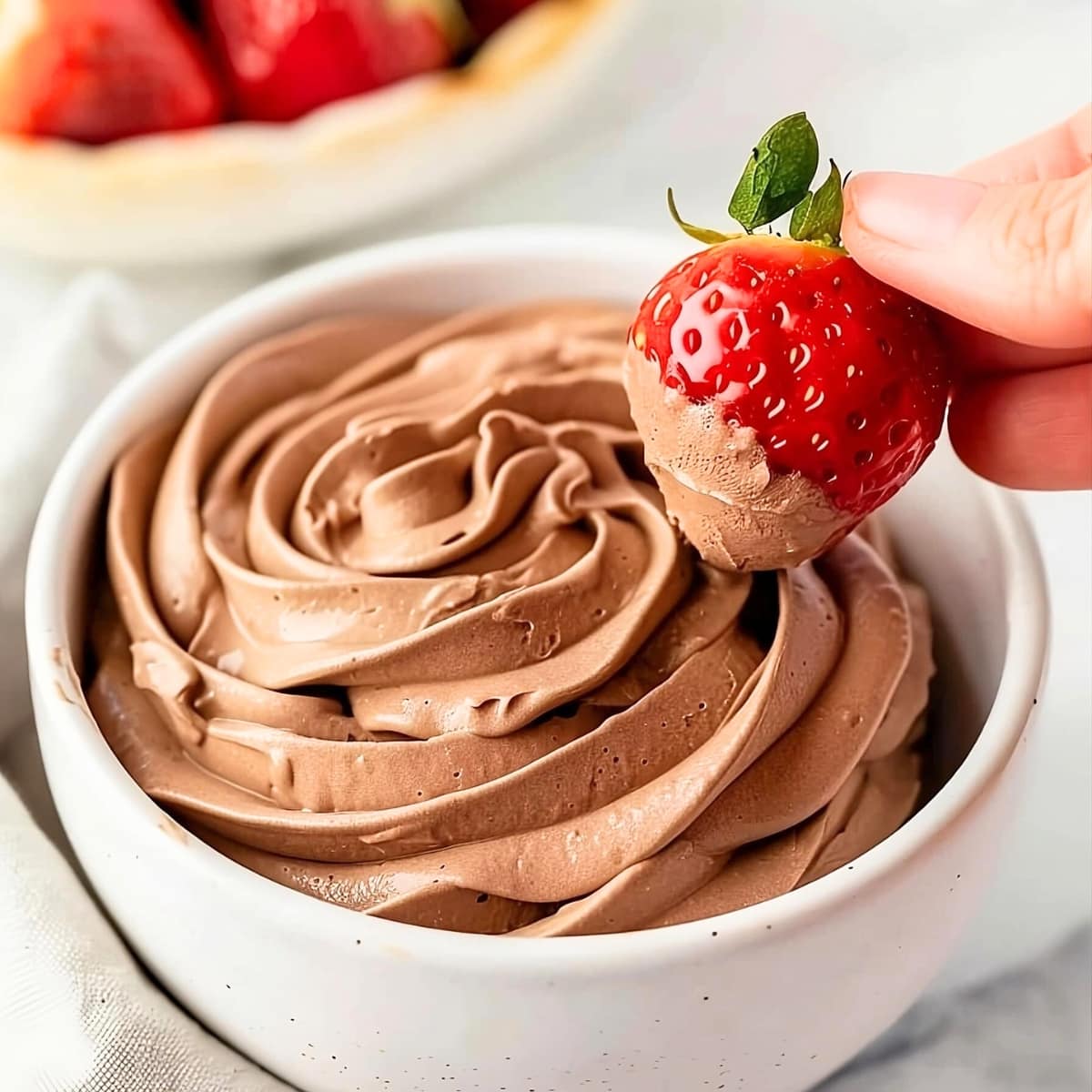 Fresh strawberry dipped on a bowl of chocolate whipped cream.