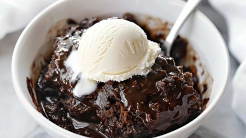 Serving of chocolate cobbler with vanilla ice cream served on a white bowl with spoon.