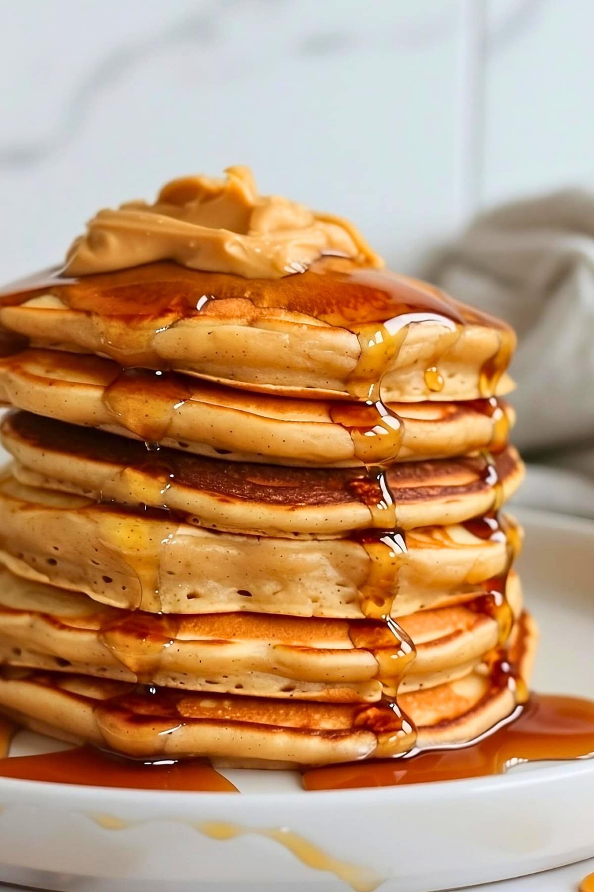Stack of peanut butter pancakes in a plate with maple syrup and peanut butter spread.