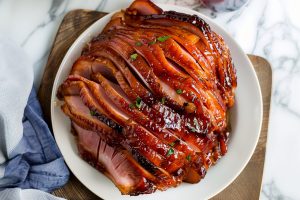 Sweet and savory homemade Coca-Cola glazed ham in a plate on a white marble table