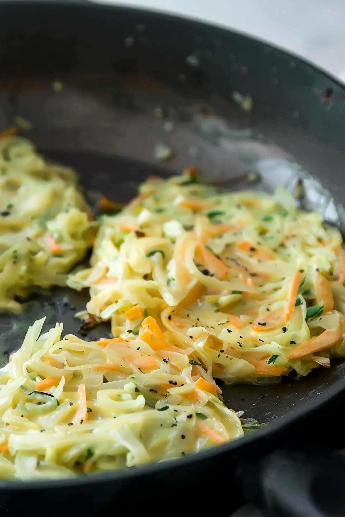 Battered cabbage and carrot fritters cooked in a black skillet