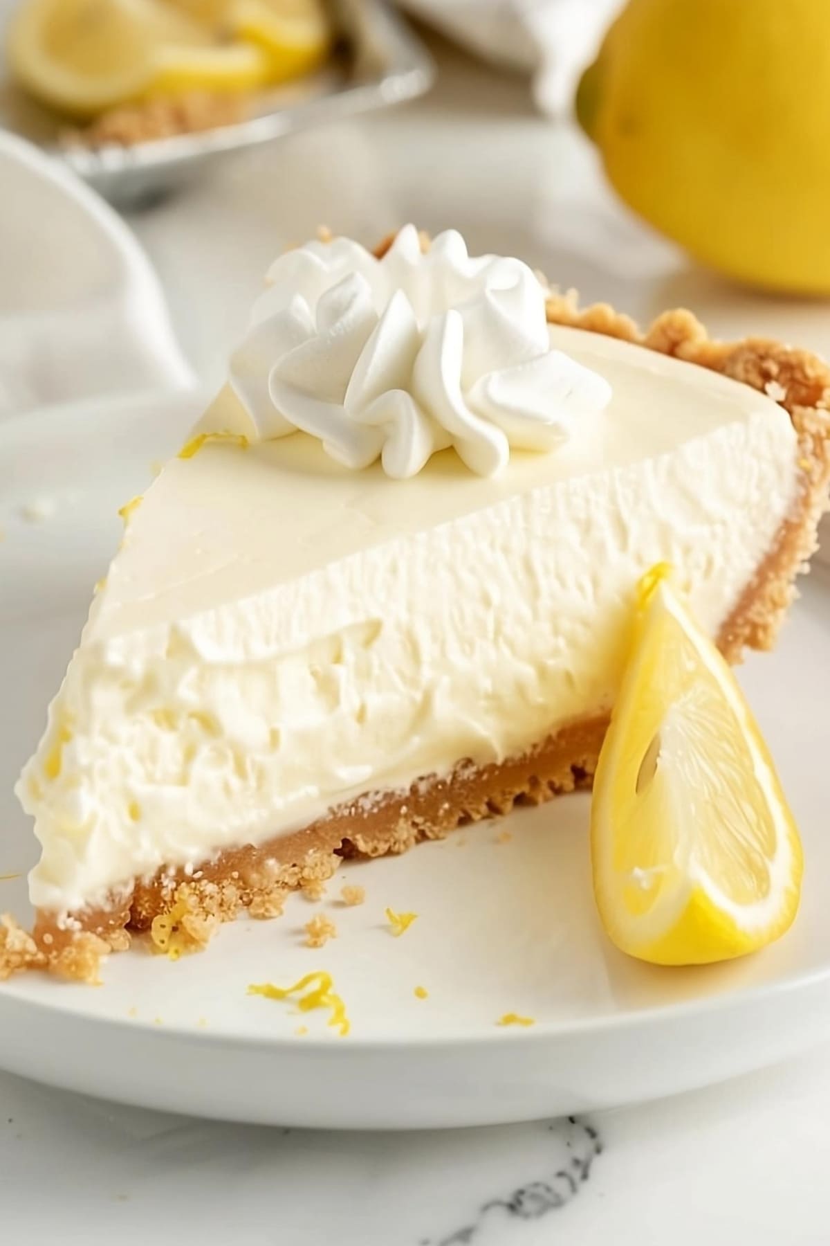 Cream Cheese Lemonade Pie garnished with dollop of whipped cream and lemon wedge slice on the side served on a white plate.
